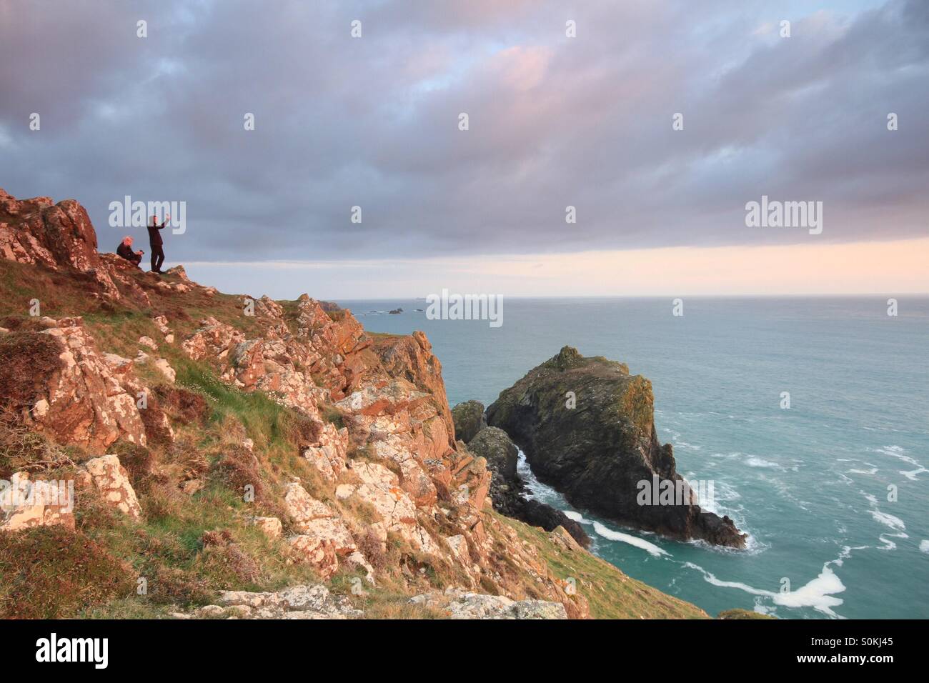 Two people taking selfies on a cliff side at sunset. Overlooking the ocean. - Smartphone Captured Stock Image