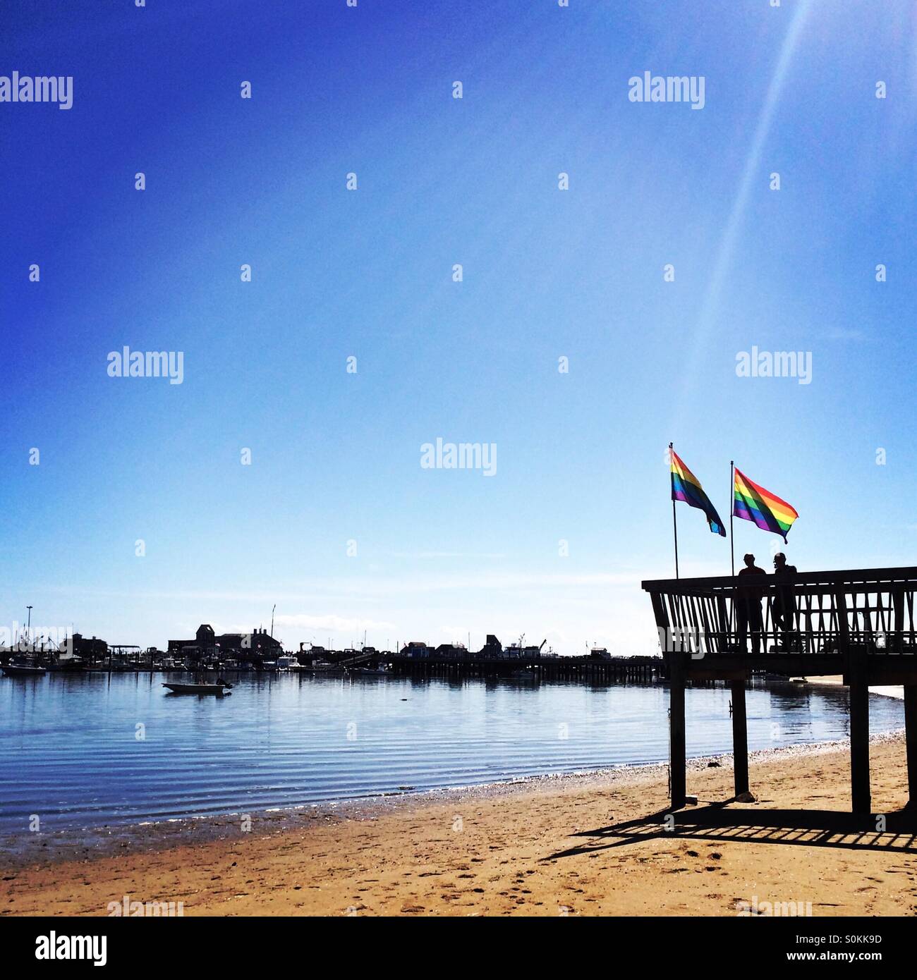 Two people stand under rainbow flags and look out towards the water in Provincetown, Massachusetts Stock Photo