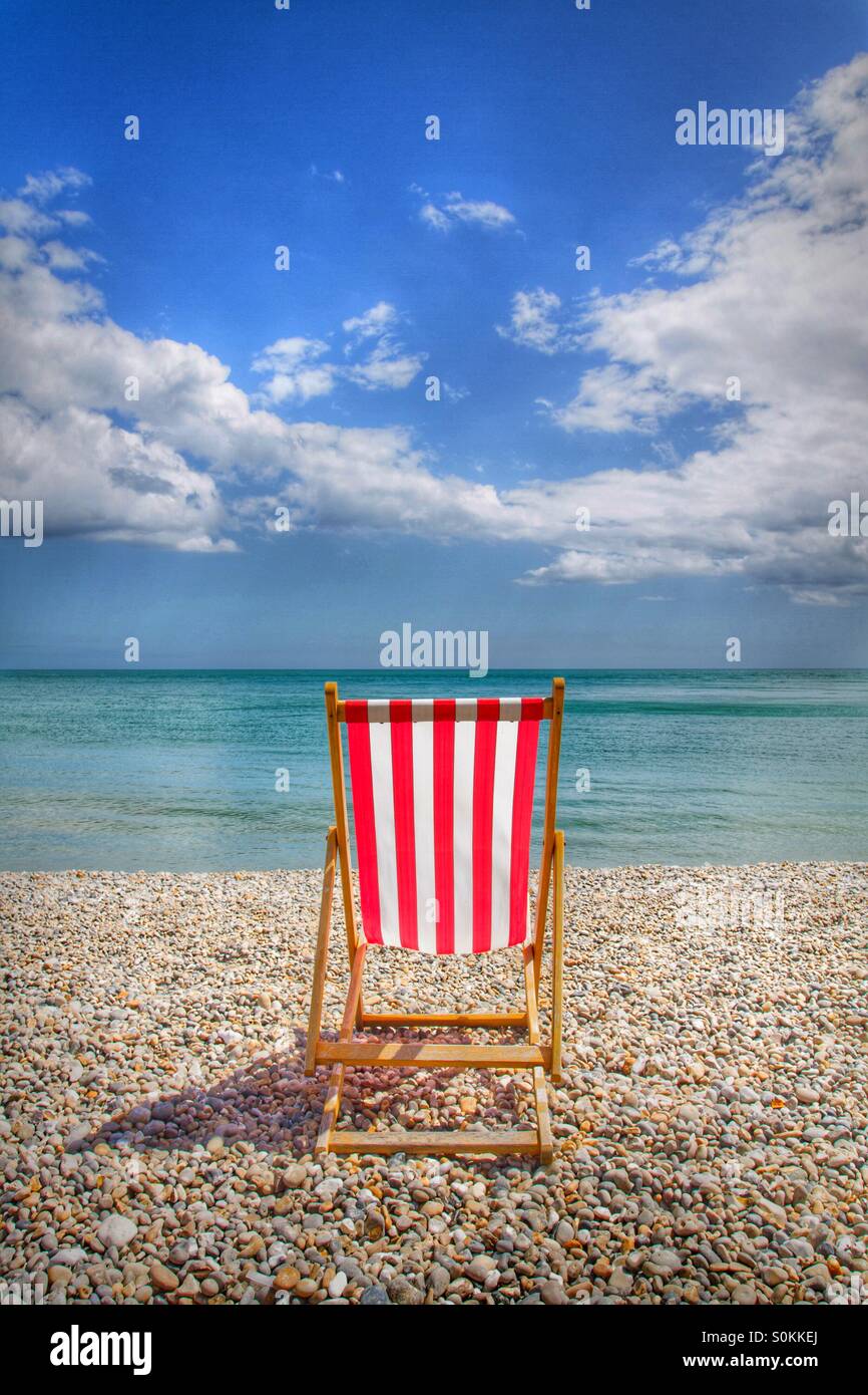 A single red and white striped Deckchair on a pebble beach facing the sea on a lovely summer's day. - Smartphone Captured Stock Image