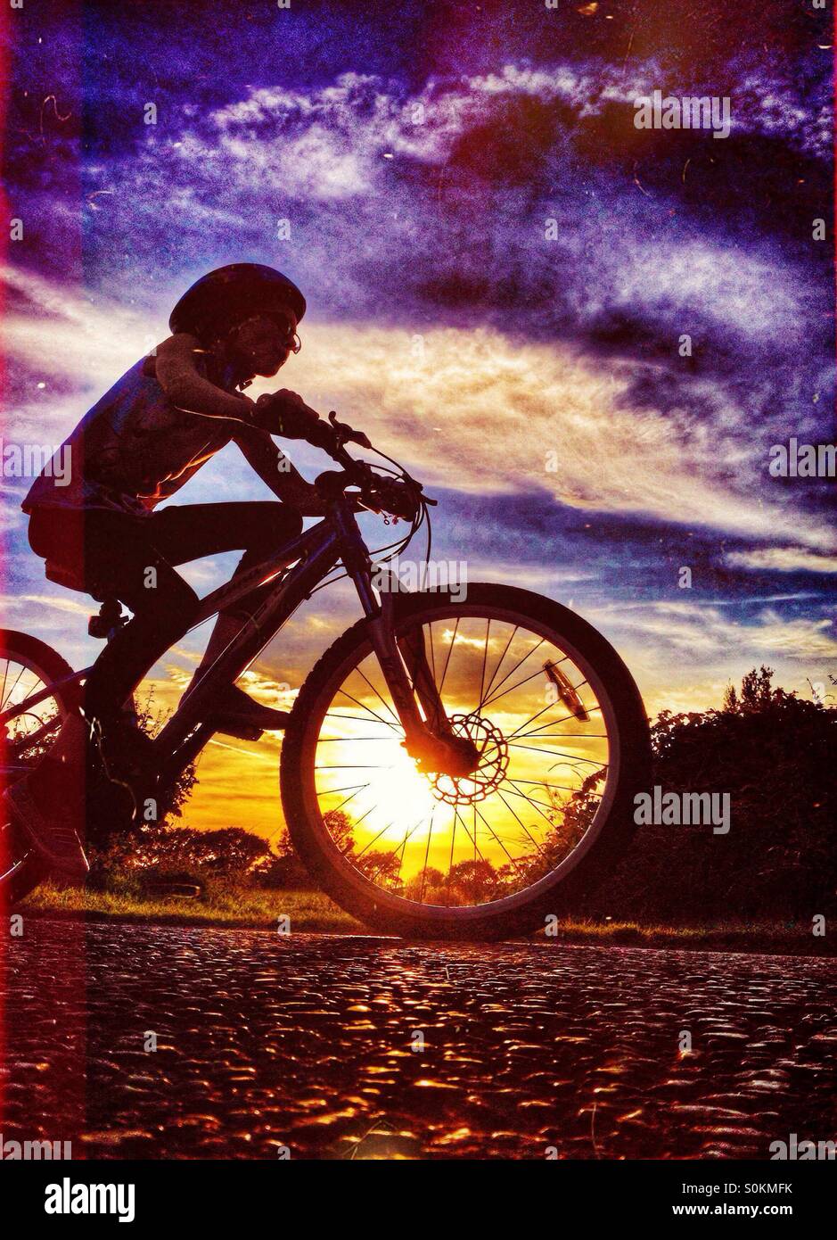 Young girl riding bike silhouetted against setting sun Stock Photo