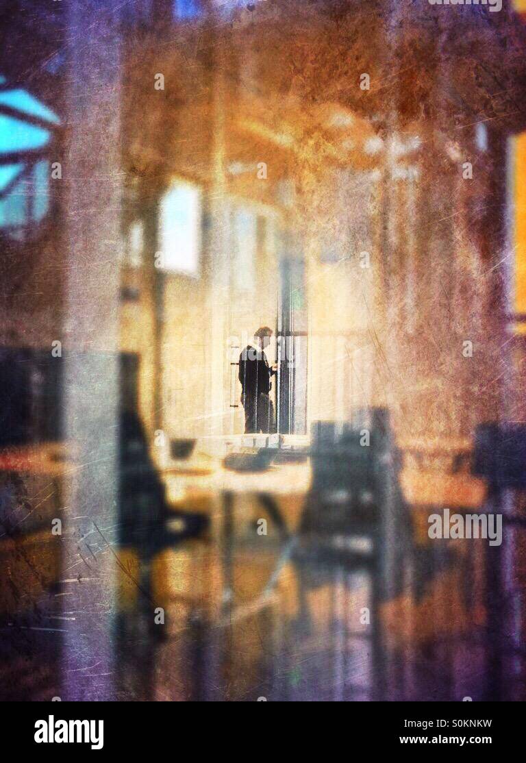 Lone man seen through an office window, standing at the entrance of a meeting room. - Smartphone Captured Stock Image