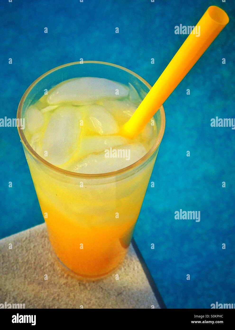 An icy tropical drink sitting on the edge of a swimming pool diving board with the blue water in the background. - Smartphone Captured Stock Image
