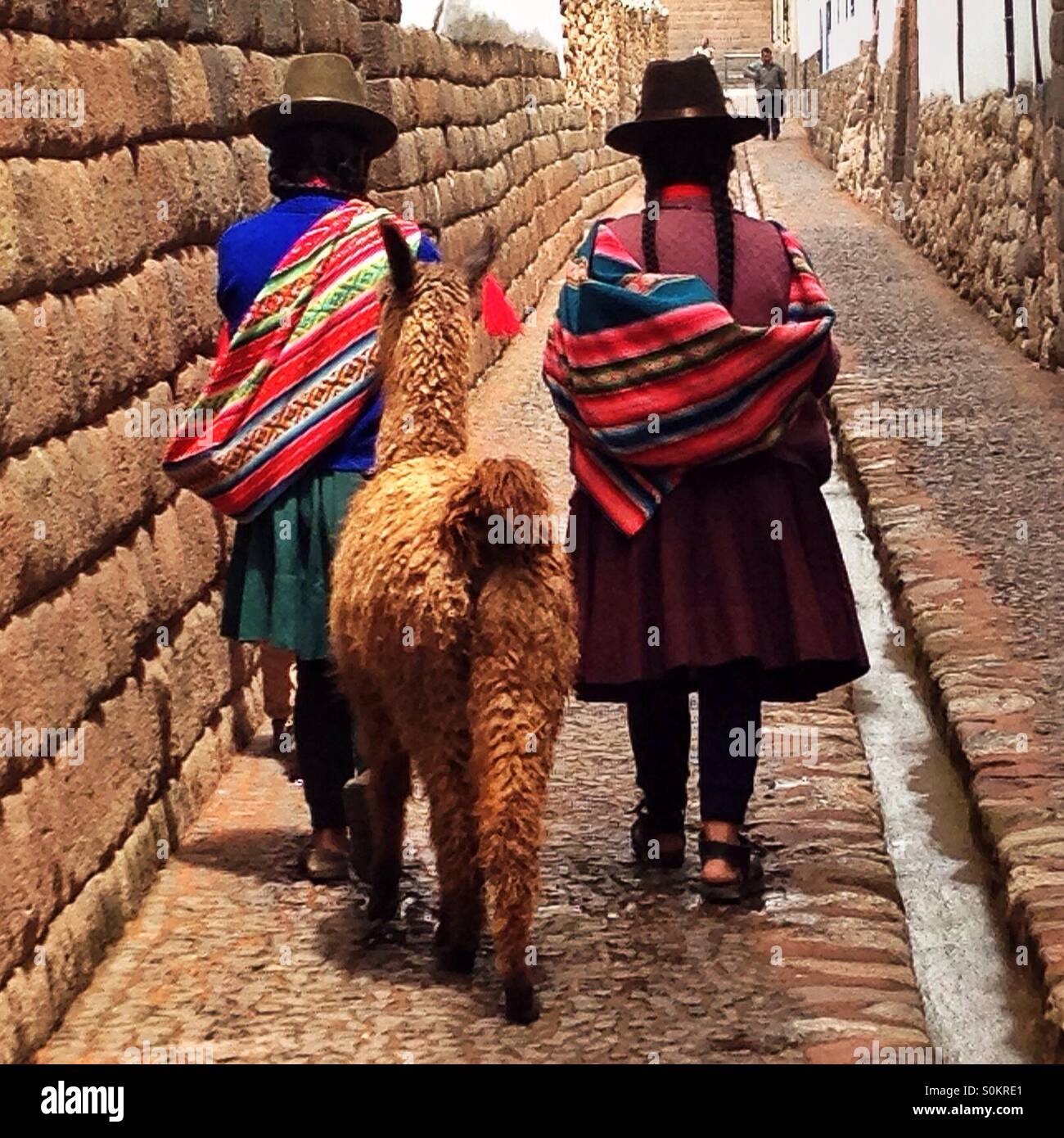 Two Andean women walk through the streets of Cusco, Peru with a llama Stock Photo