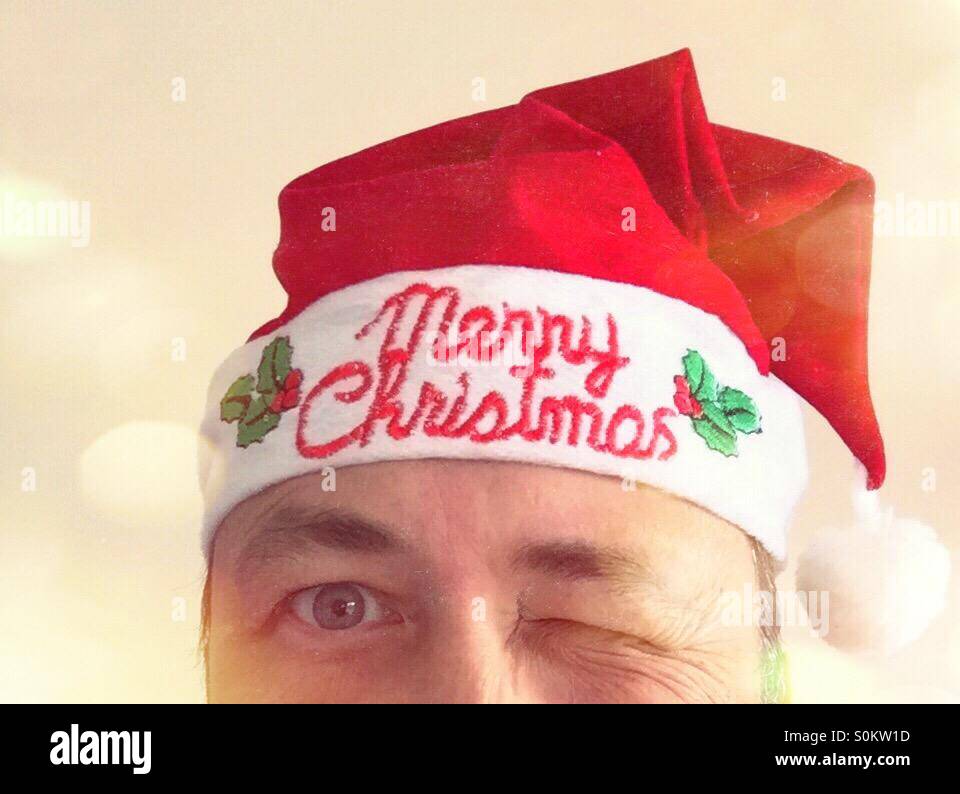 Partial portrait of a man winking, with a Christmas hat. Text: Merry Christmas - Smartphone Captured Stock Image