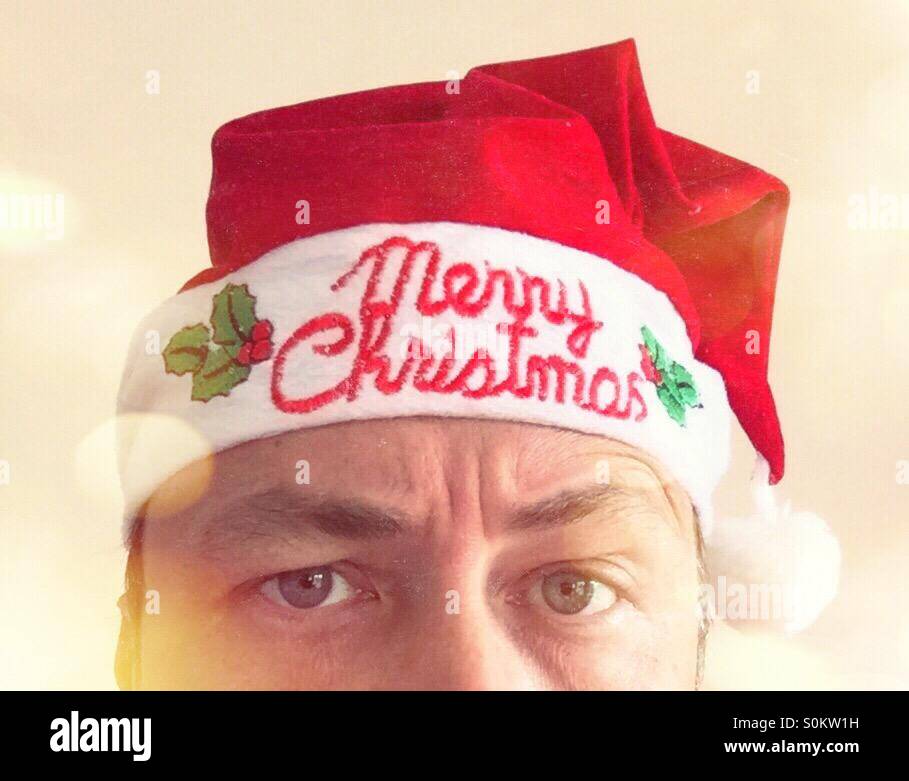 Partial portrait of a man looking bored, with a Christmas hat. Text: Merry Christmas - Smartphone Captured Stock Image