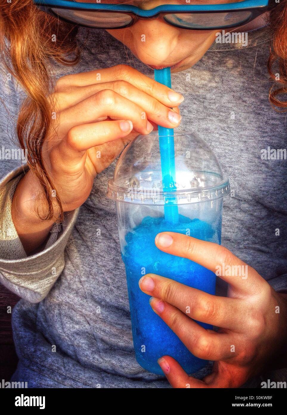 Young girl wearing blue glass frames drinking blue slush Stock Photo