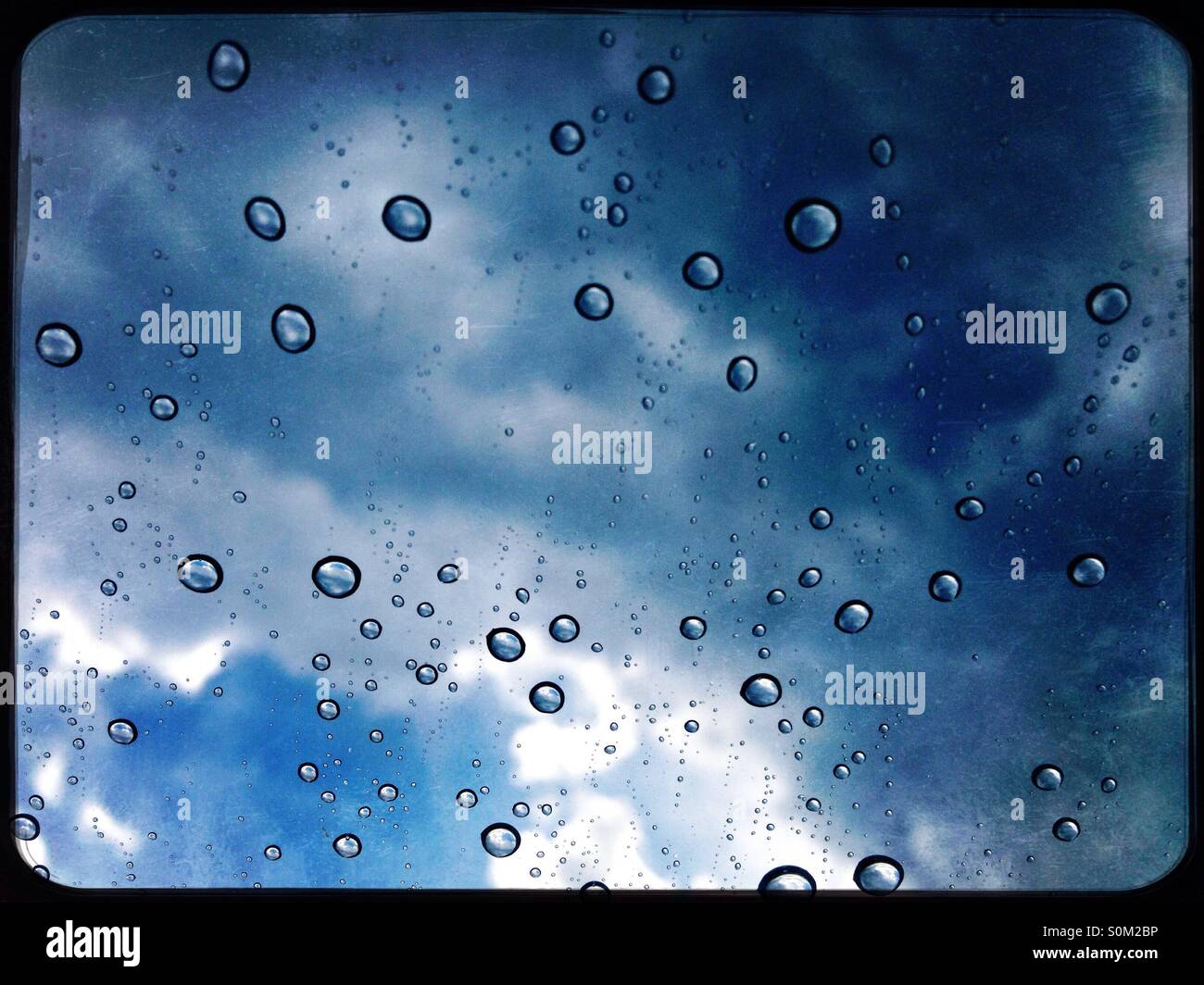 Rain droplets beaded on window with sky in background Stock Photo