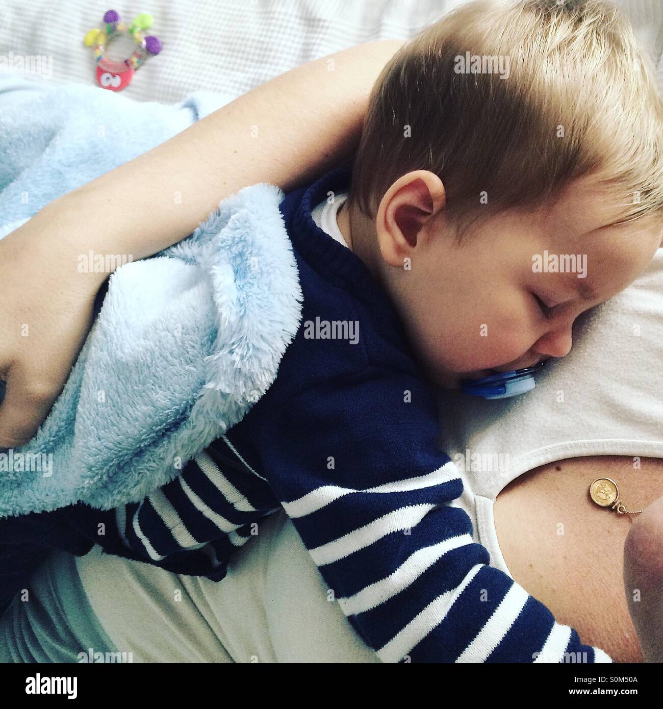 Tired 9 months old baby boy taking a nap on top of his mom . Stock Photo