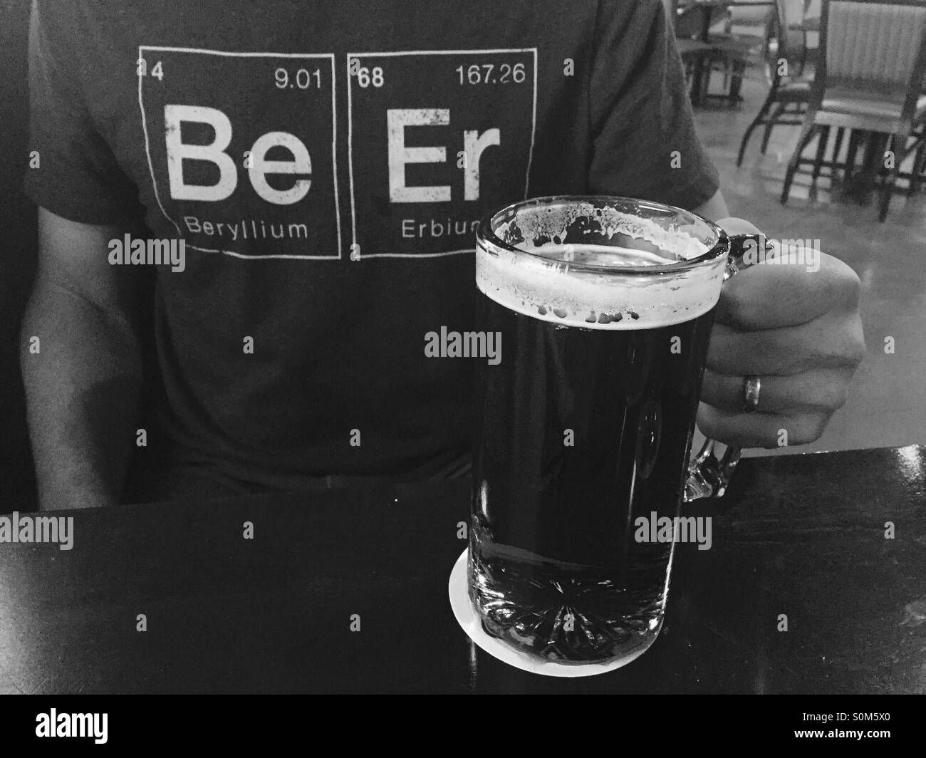 A hand holds a frosty mug of beer. Behind the beer you see a geeky science shirt that spells out the word beer. Stock Photo