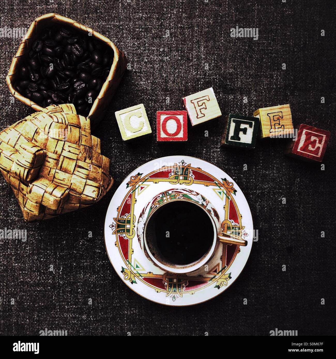 Coffee cup in fine porcelain next to word 'coffee' spelled in building blocks and box full of roasted coffee beans - Smartphone Captured Stock Image