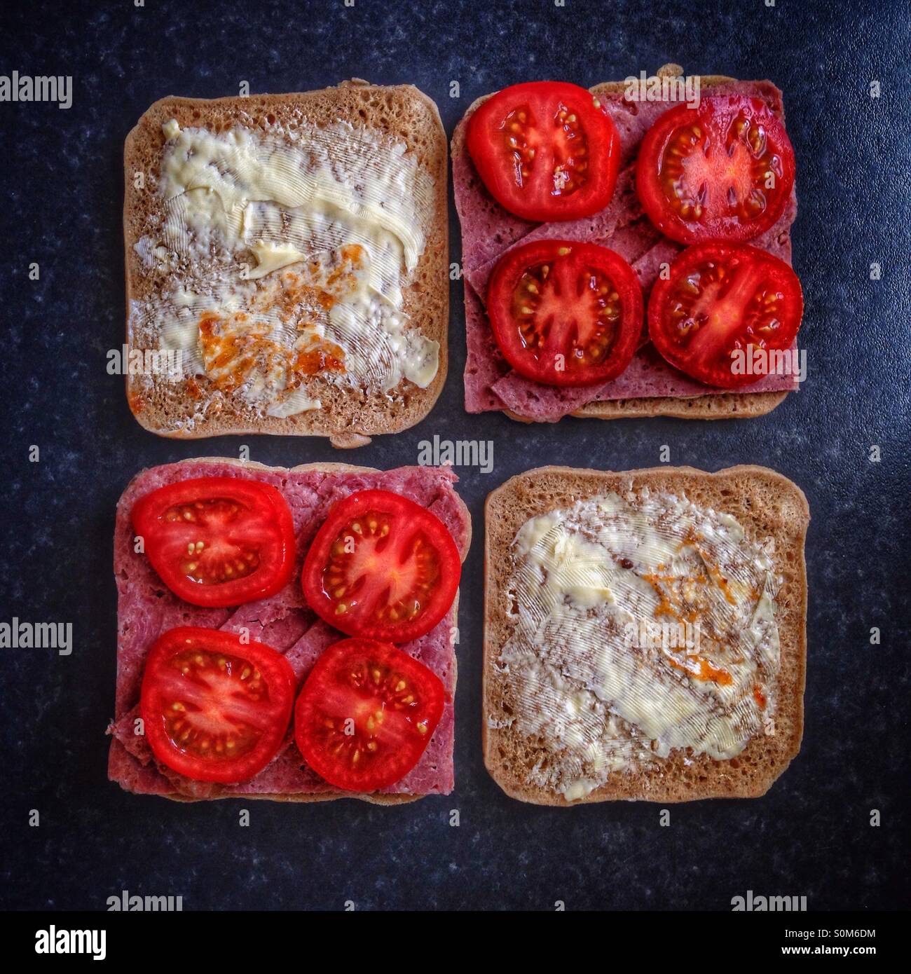 All square. Two sandwiches in square bread being prepared; with tomatoes, corned beef and pickle. - Smartphone Captured Stock Image