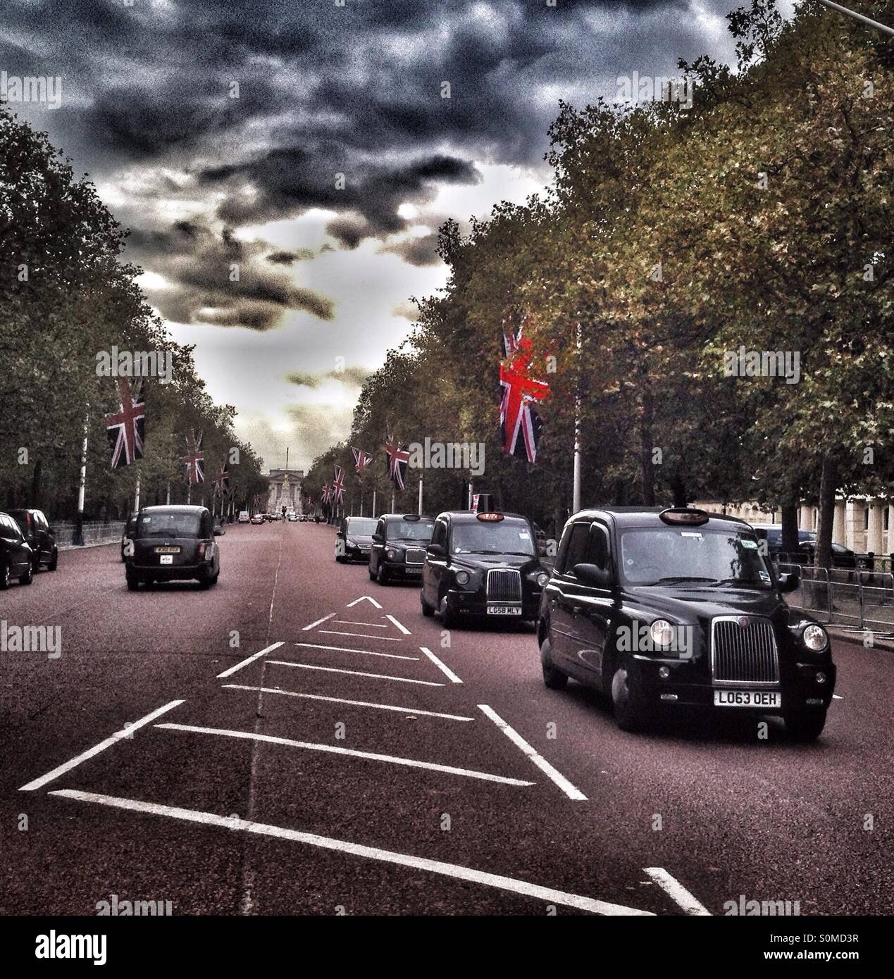 A view up the Mall toward Buckingham Palace showing London black taxis and Union Jack flags flying Stock Photo