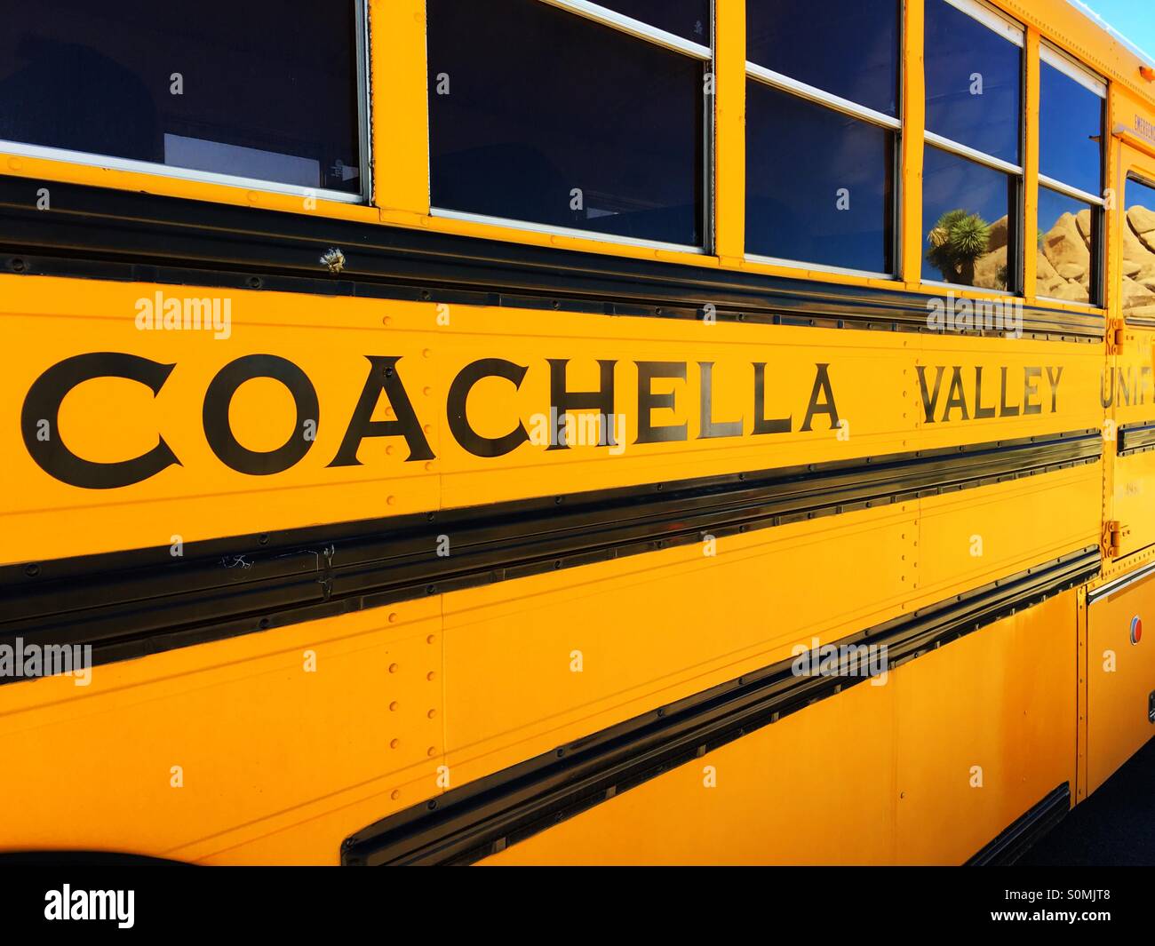 Coachella Valley yellow school bus with rocks and desert cactus reflecting in the windows in Southern California Stock Photo