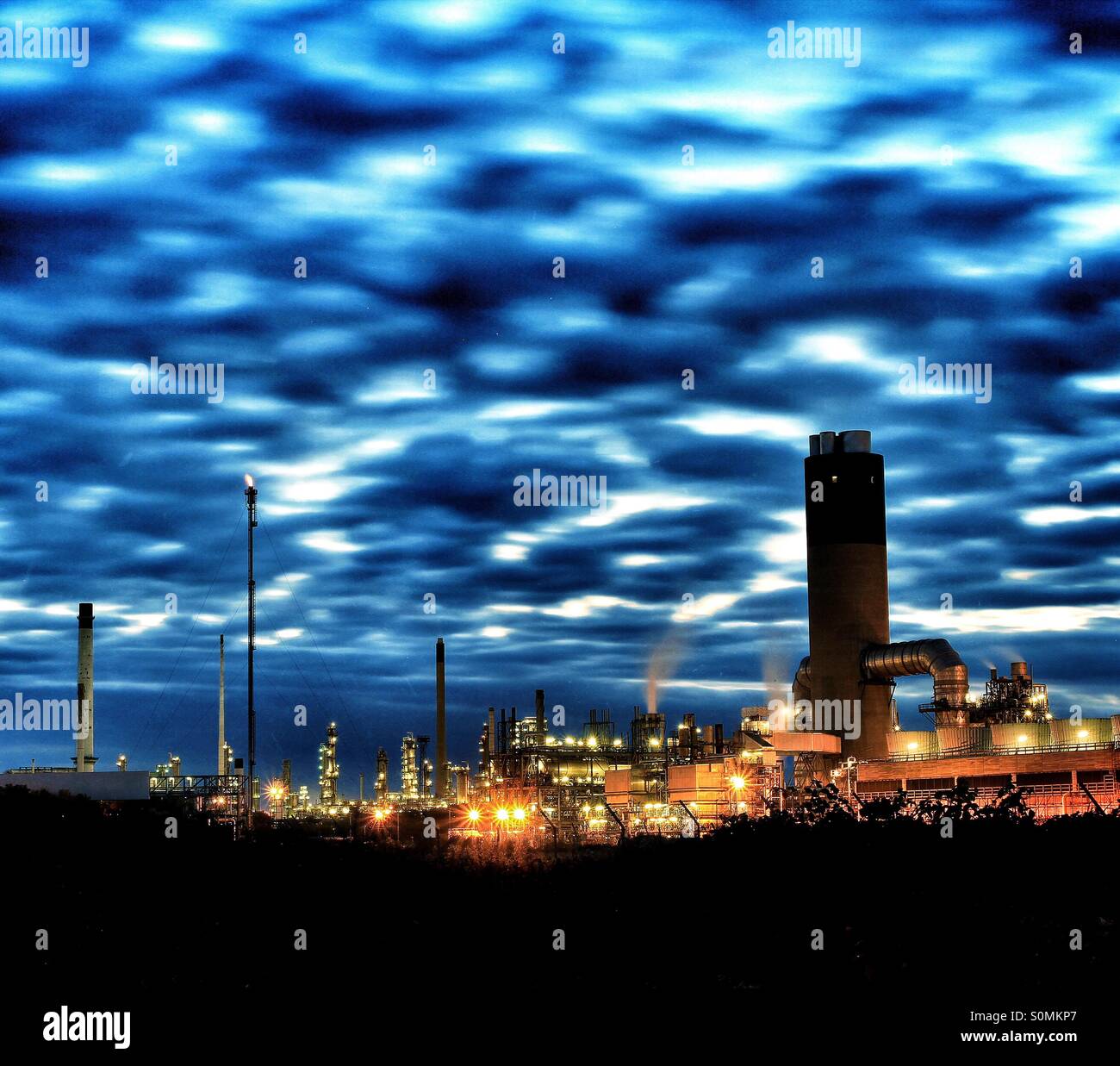 Artificial lights light up an industrial oil refinery at twilight with an attractive cloud formation. Stock Photo