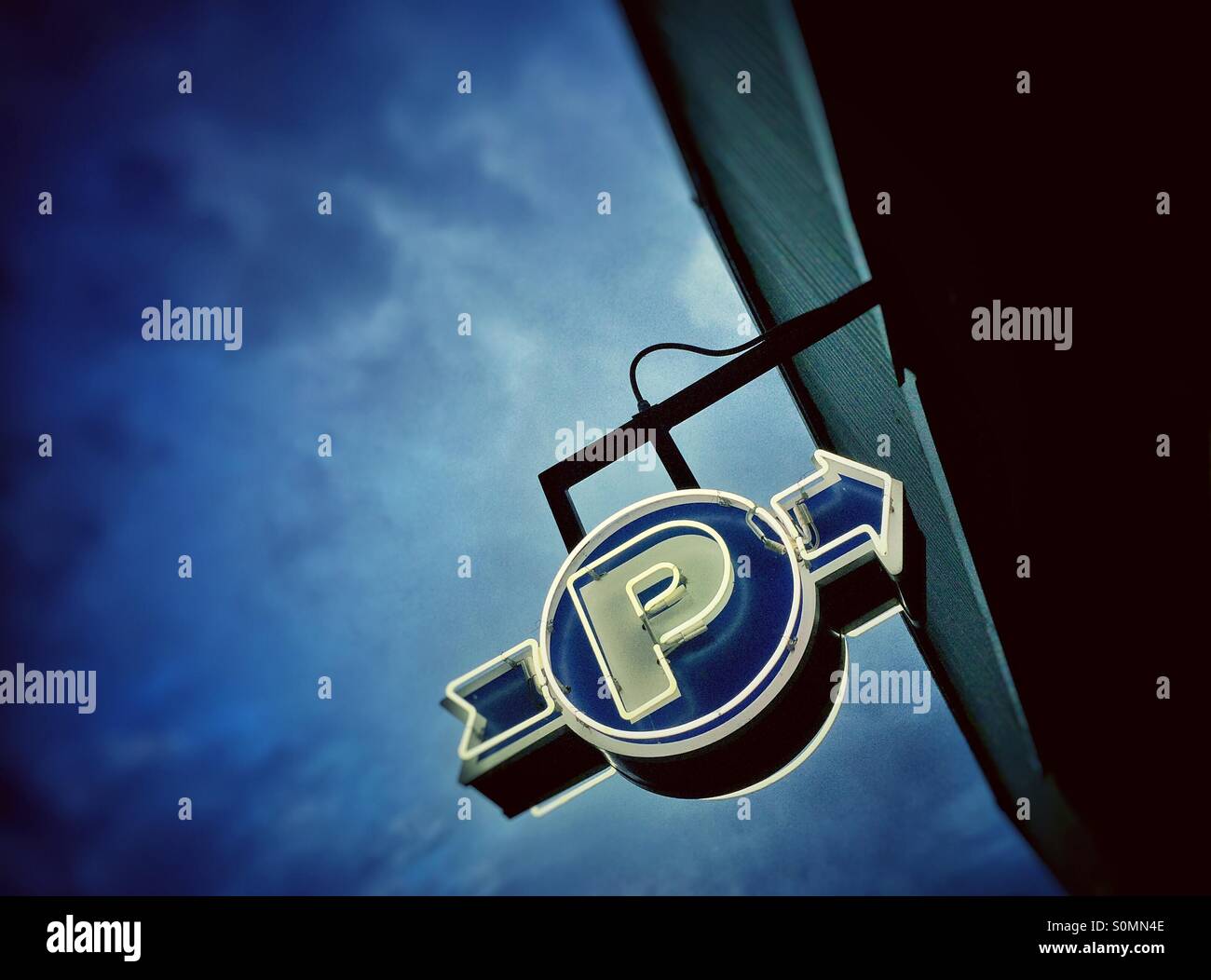 White and blue neon parking garage sign against a dark blue cloudy sky, early evening. - Smartphone Captured Stock Image