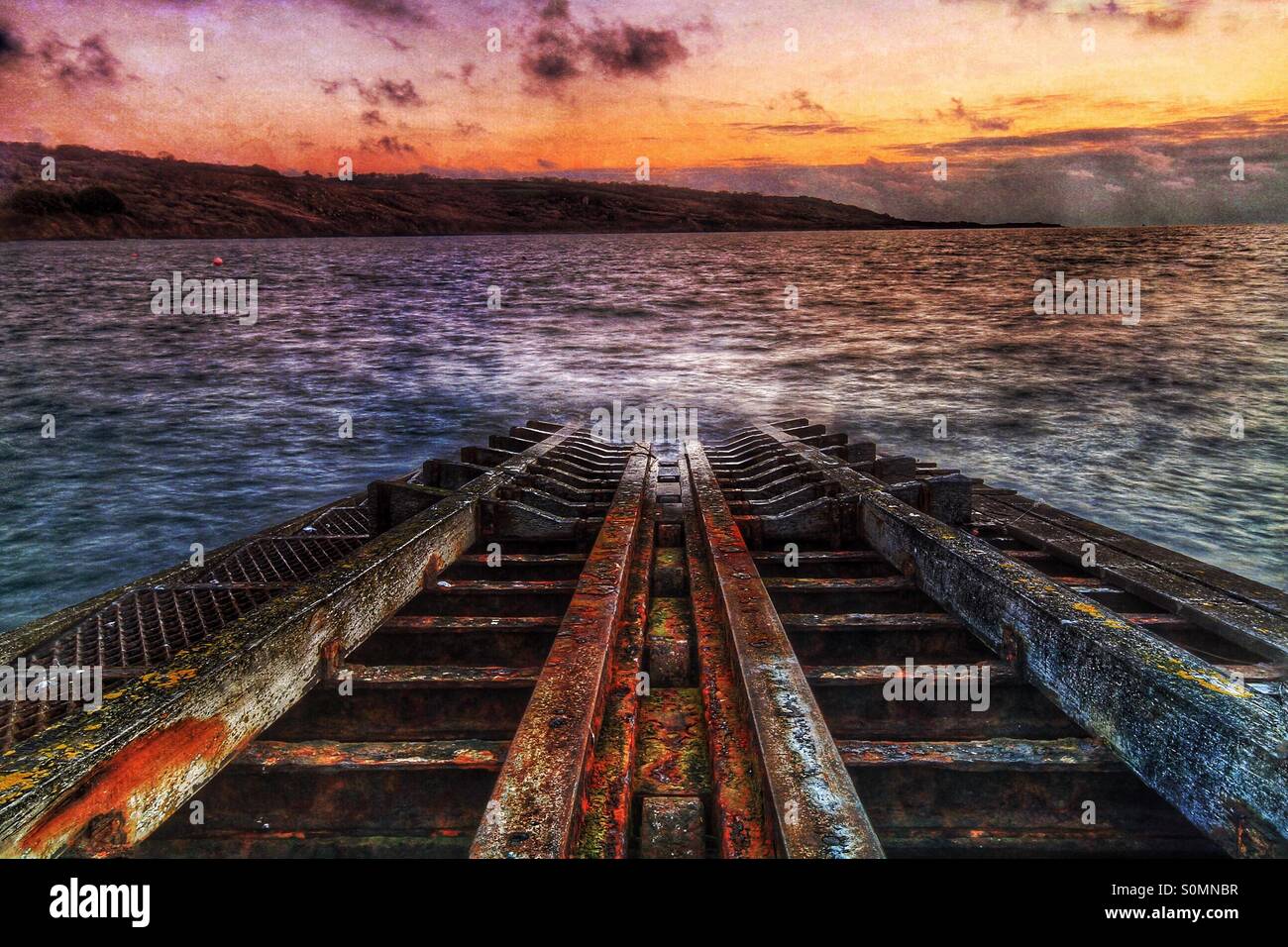 A rusted lifeboat slipway in a state of decay disappears into a steel, gray Ocean at sunrise. - Smartphone Captured Stock Image