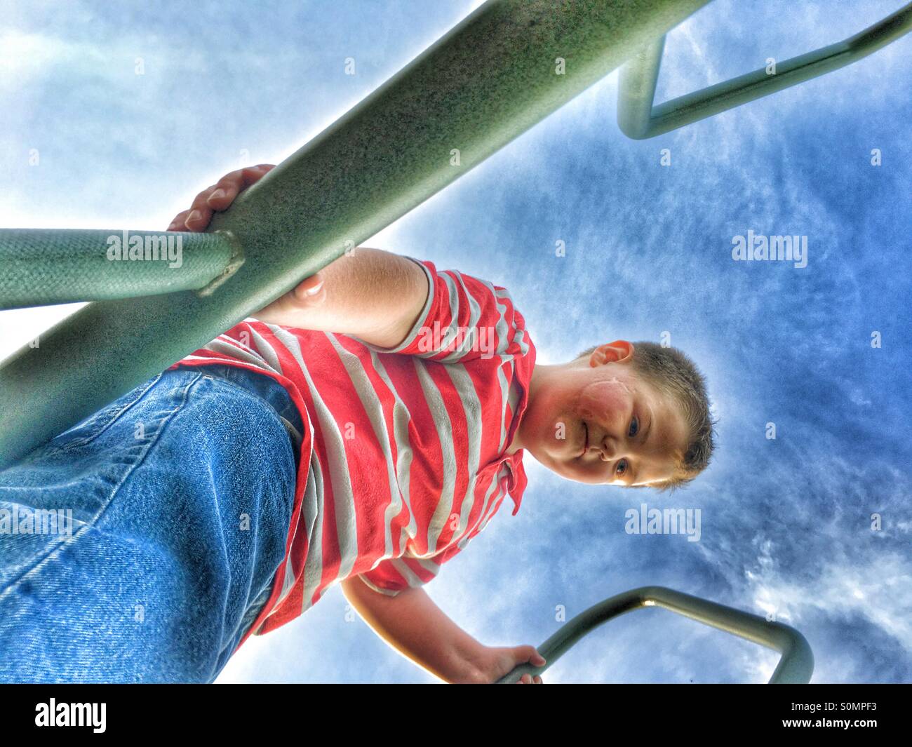 A ground view of a boy on monkey bars with blue skies as a background. - Smartphone Captured Stock Image