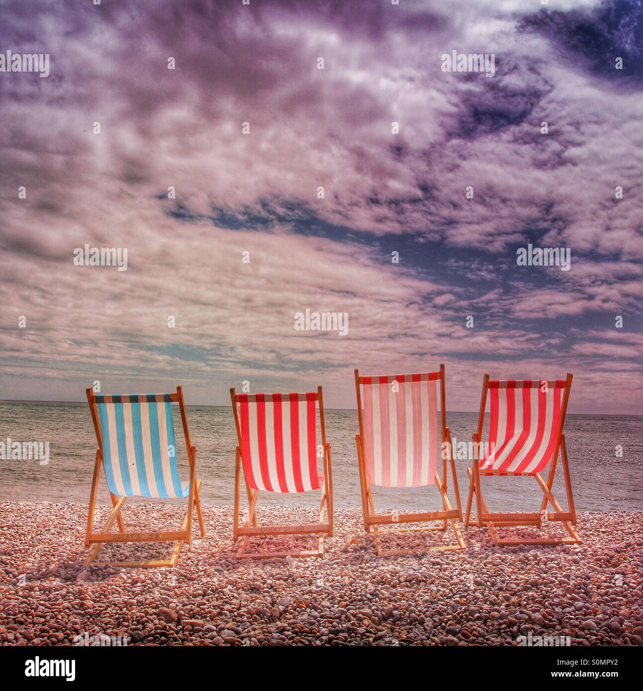Four deckchairs facing the ocean on a pebble beach on a beautiful summer's day. - Smartphone Captured Stock Image