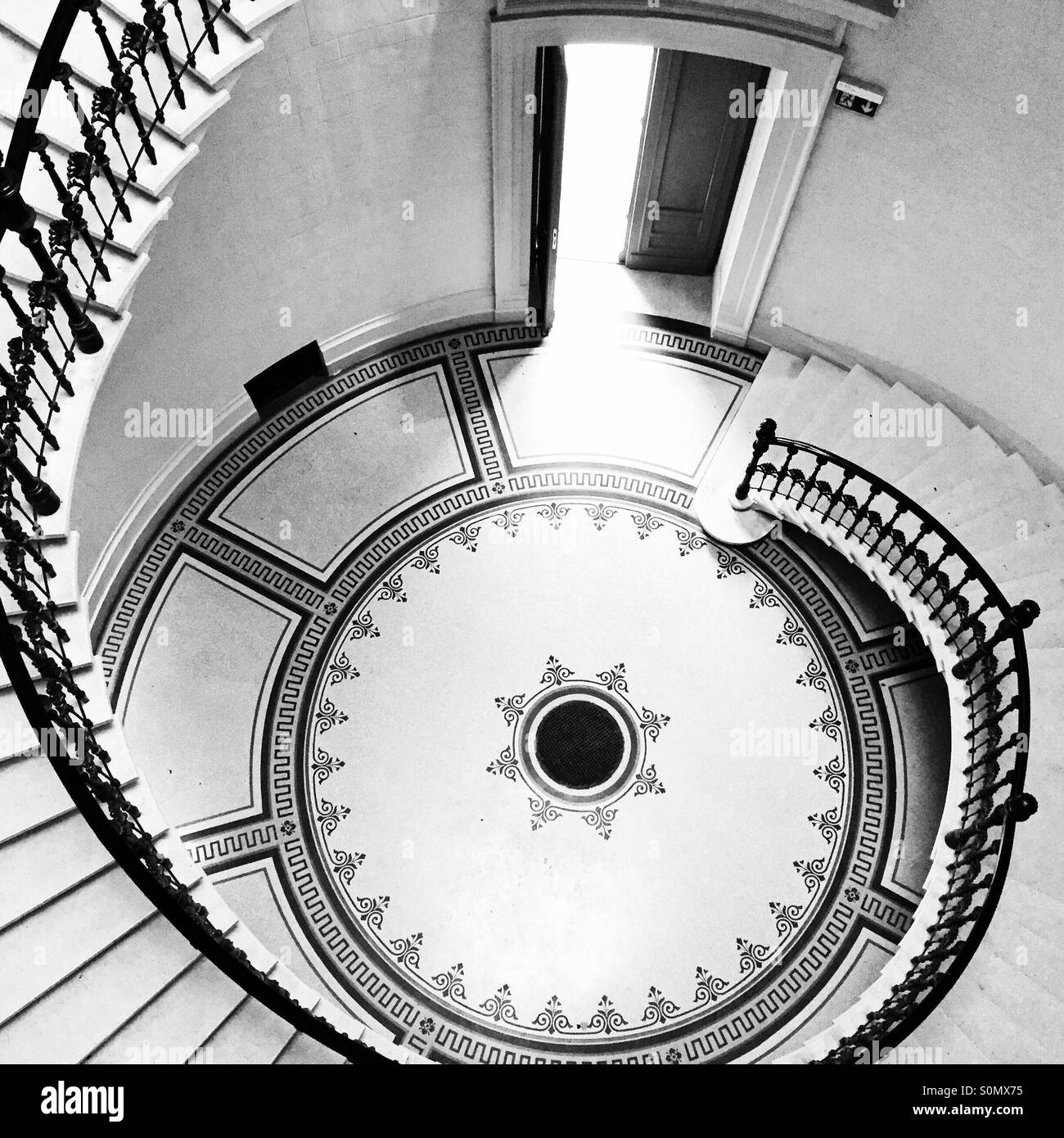 Spiral stone staircase with light shining through open door below. - Smartphone Captured Stock Image