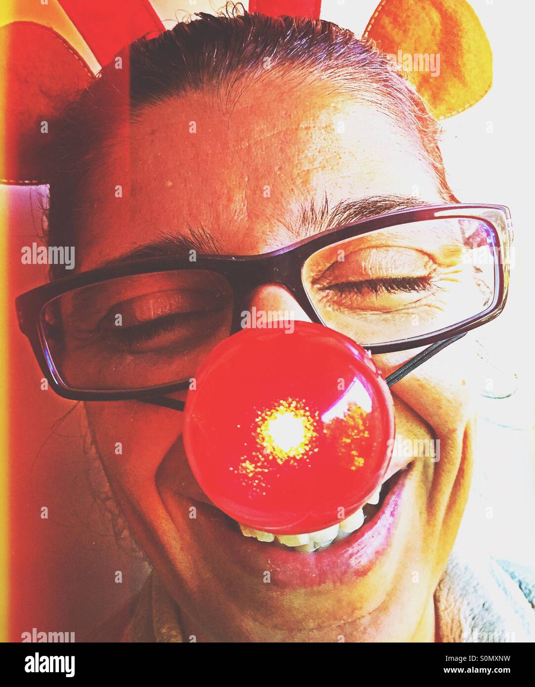 Portrait of a woman laughing and having fun with a blinking red nose and toy reindeer antlers on her head. - Smartphone Captured Stock Image