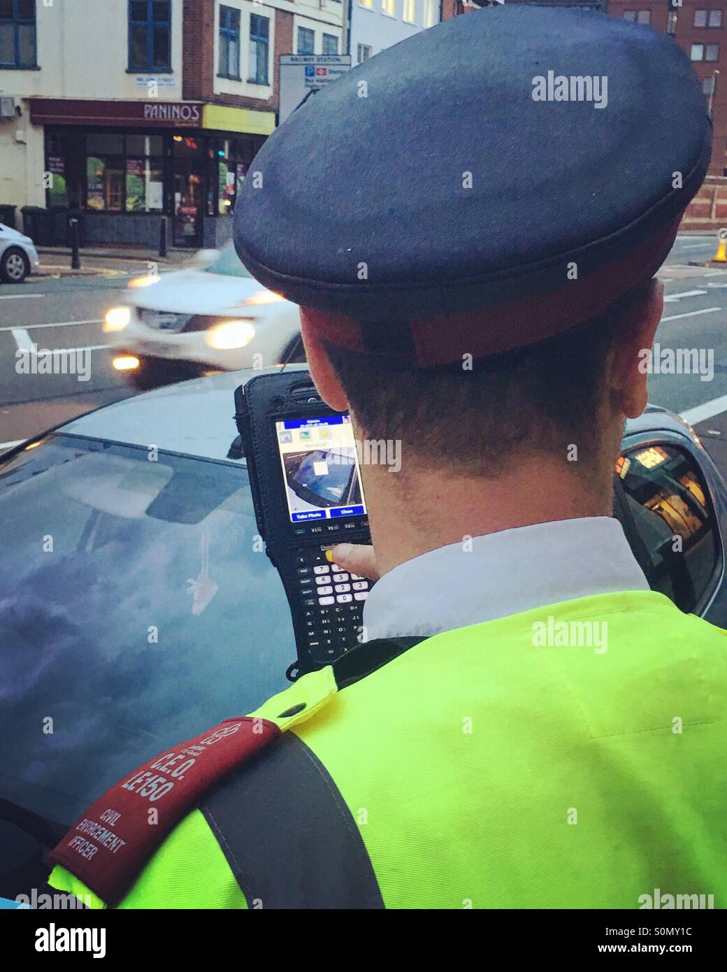 Rear view of a Parking Enforcement Officer photographing and applying a penalty ticket to a car. - Smartphone Captured Stock Image