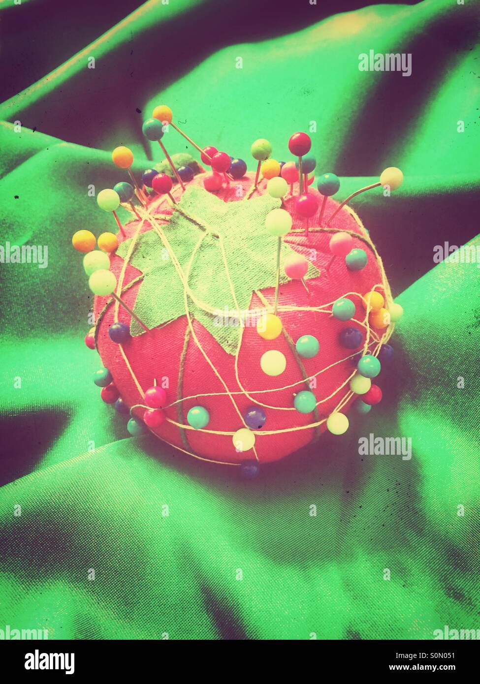 Pin cushion shaped like a tomato sitting on green silk fabric Stock