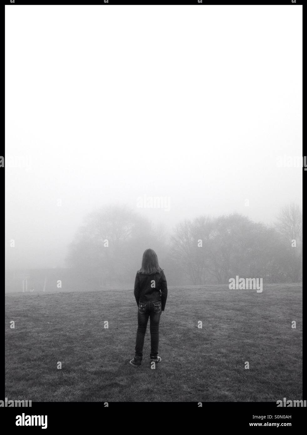 Child stood in field looking into the distance on a foggy day Stock Photo