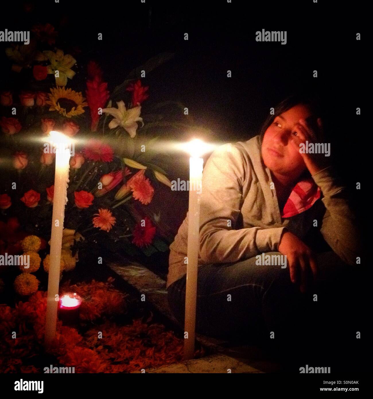 A girl sits on a tomb during All Souls Day in Mexico City. The Day of the Dead celebration mixes Pre-Hispanic traditions with the European tradition of the Catholic All Souls Day. - Smartphone Captured Stock Image
