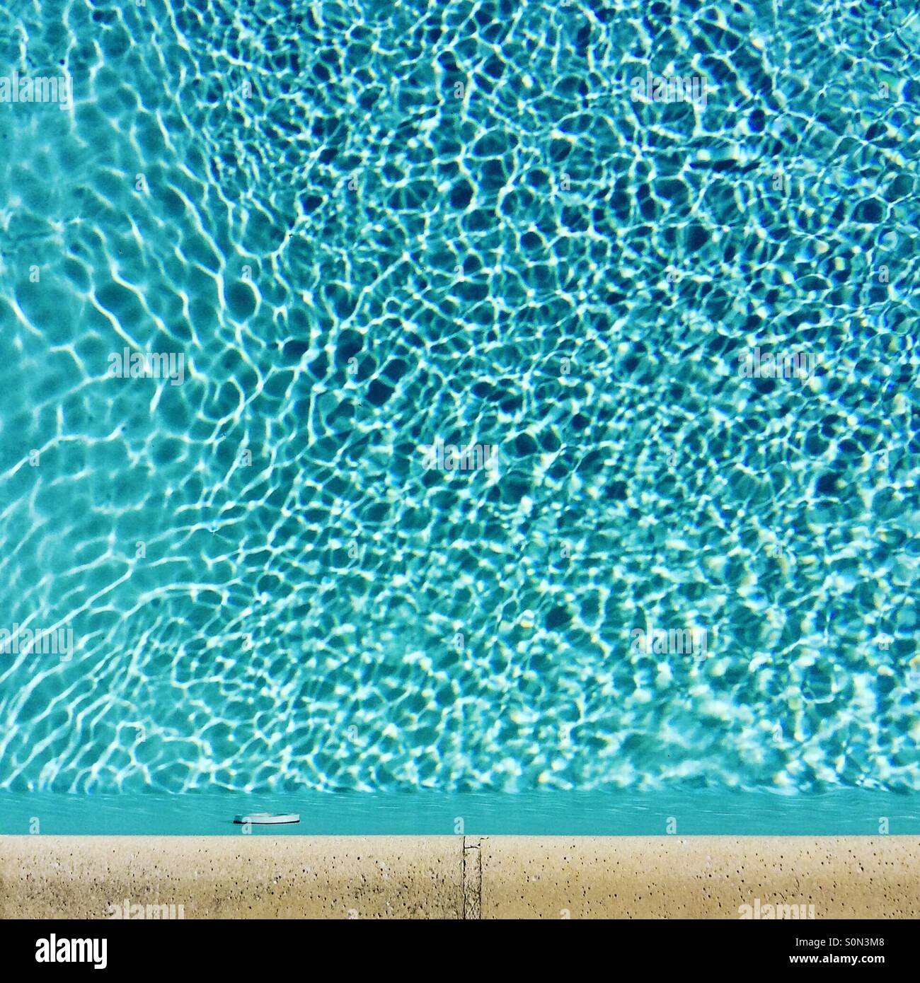 Standing on the side of a swimming pool looking down at the ripples in sunlight Stock Photo