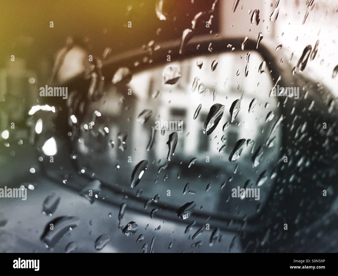 Rearview mirror of a car seen through raindrops on the side window. - Smartphone Captured Stock Image