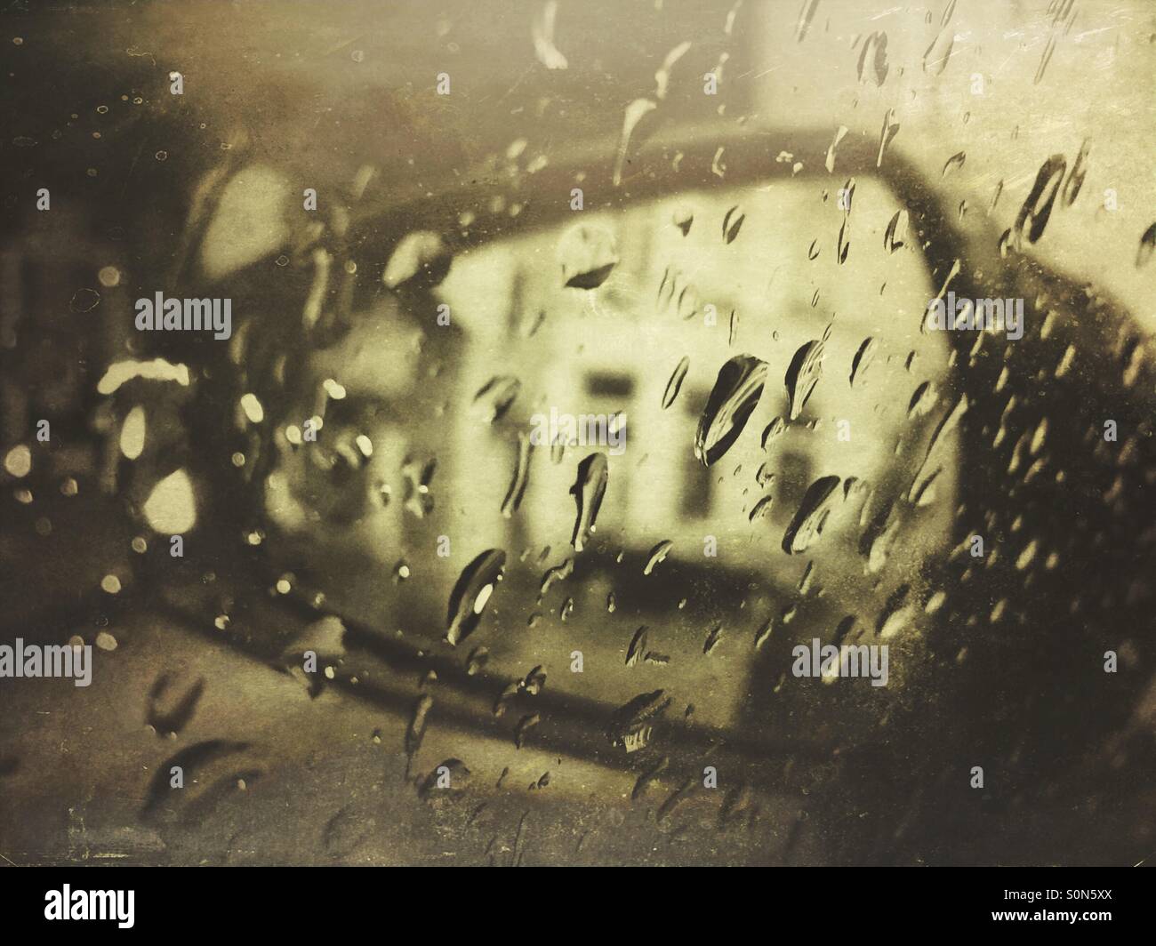 Rearview mirror of a car seen through raindrops on the side window. - Smartphone Captured Stock Image