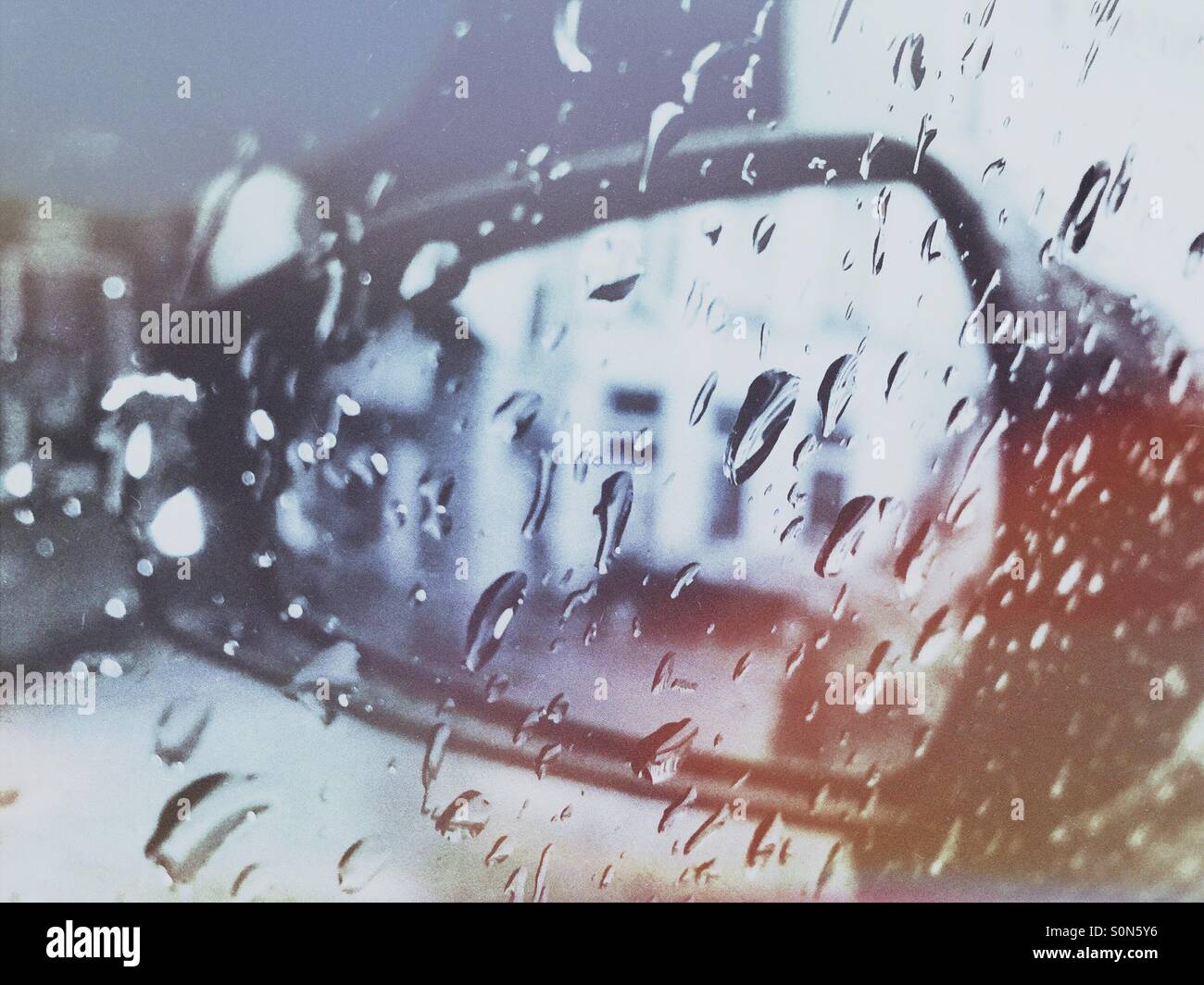 Rearview mirror of a car seen through raindrops on the side window. - Smartphone Captured Stock Image