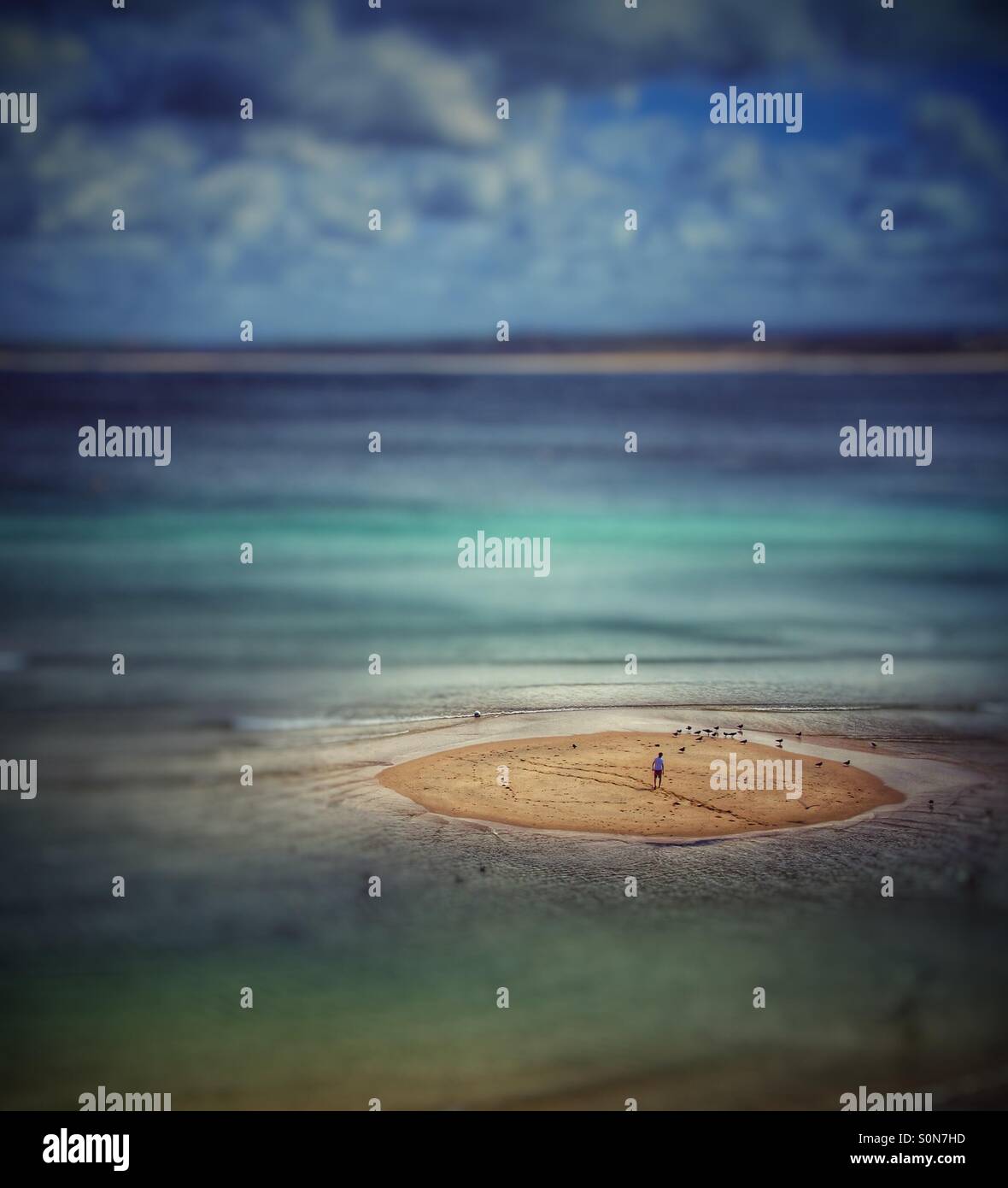 A lone man stranded on an isolated sandbank as the ocean surrounds him. - Smartphone Captured Stock Image