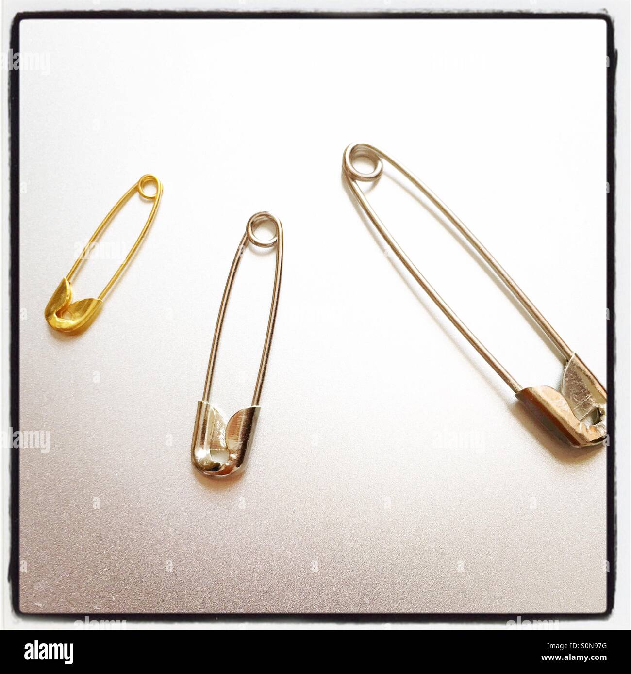 Three safety pins of differing size. Stock Photo