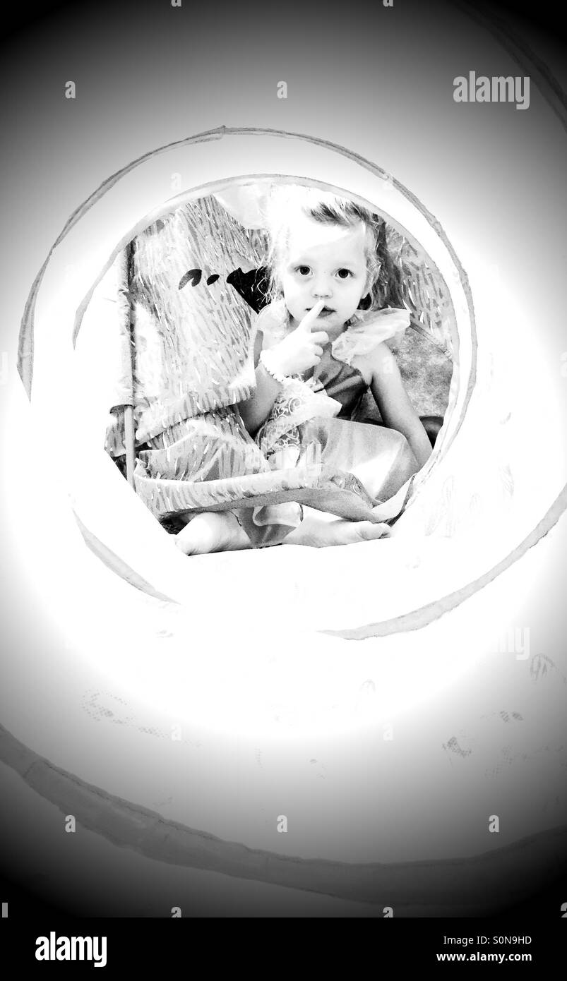 End of the tunnel. Little girl hiding in a tent with an attached tunnel, with her finger up to her lip saying shhh! Stock Photo