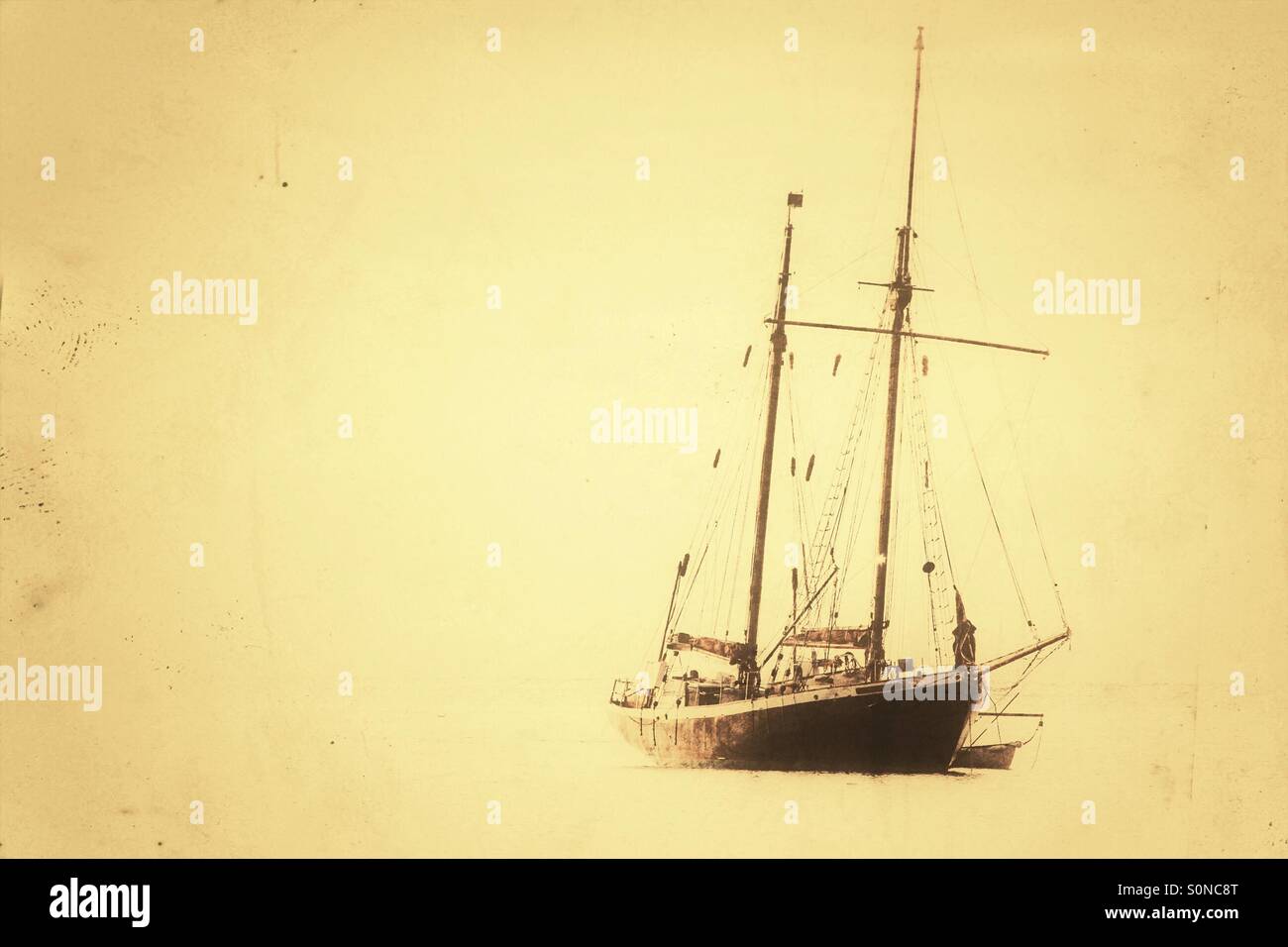 A yacht with two masts moored on a flat, calm Ocean with a vintage feel. - Smartphone Captured Stock Image