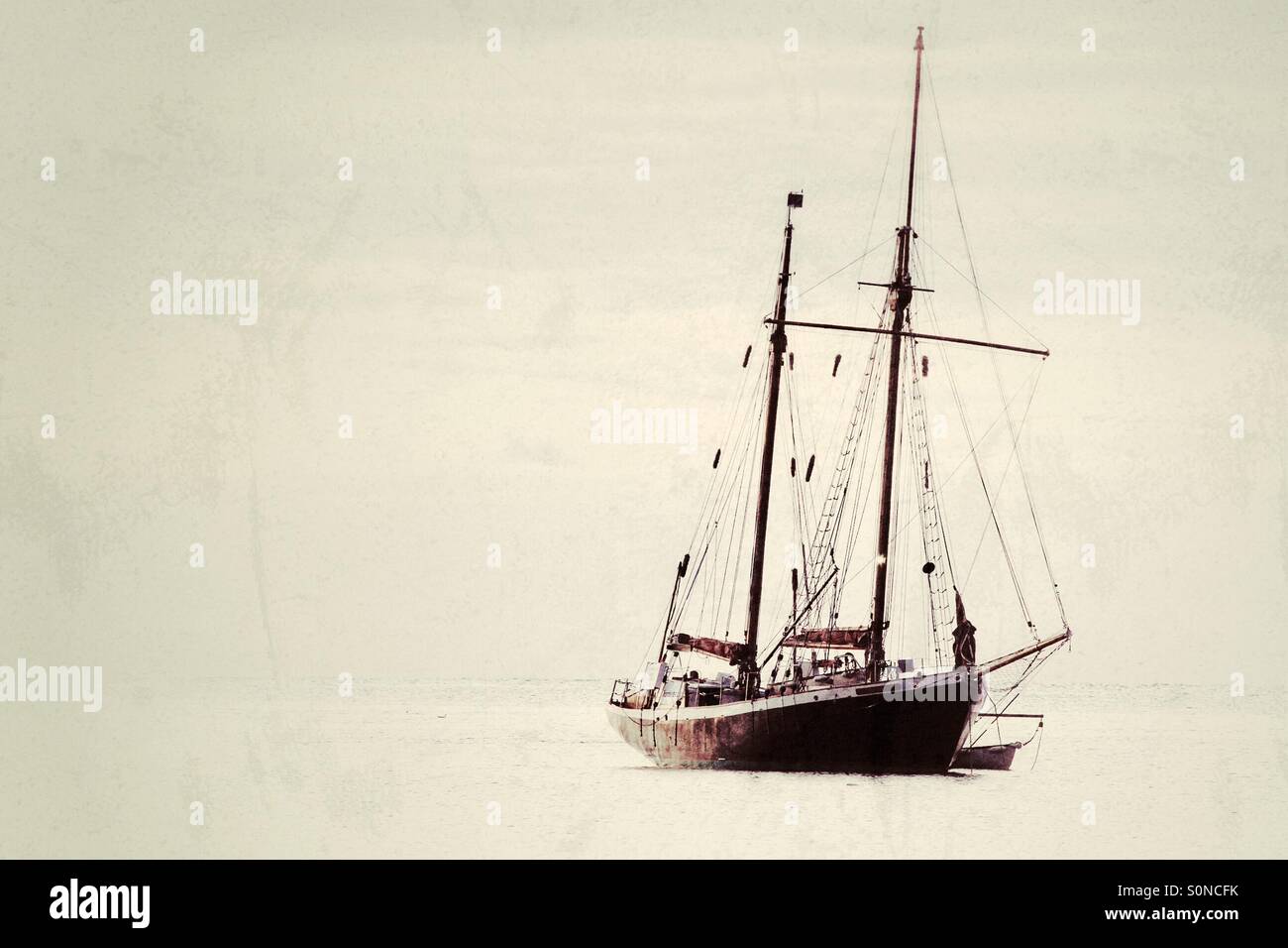 A single, twin masted yacht floating on a calm, flat Ocean. - Smartphone Captured Stock Image