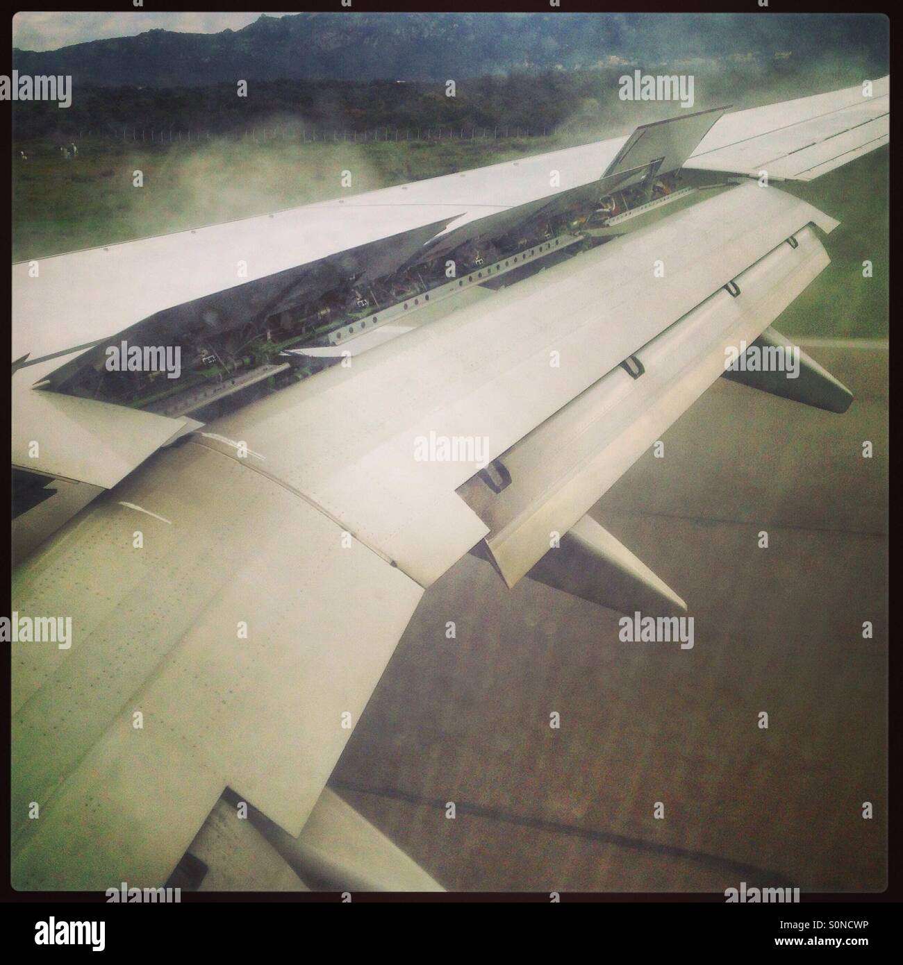 Flaps on the wing of a plane open as it lands at an airport. Stock Photo