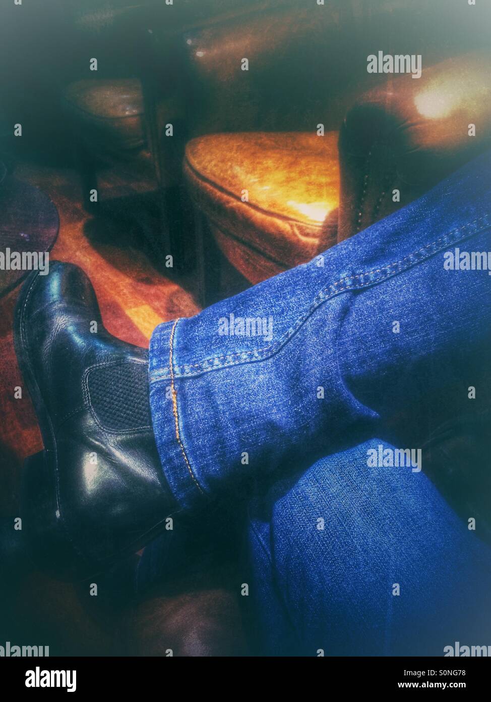 Person seated with crossed legs wearing blue jeans and black boots - Smartphone Captured Stock Image
