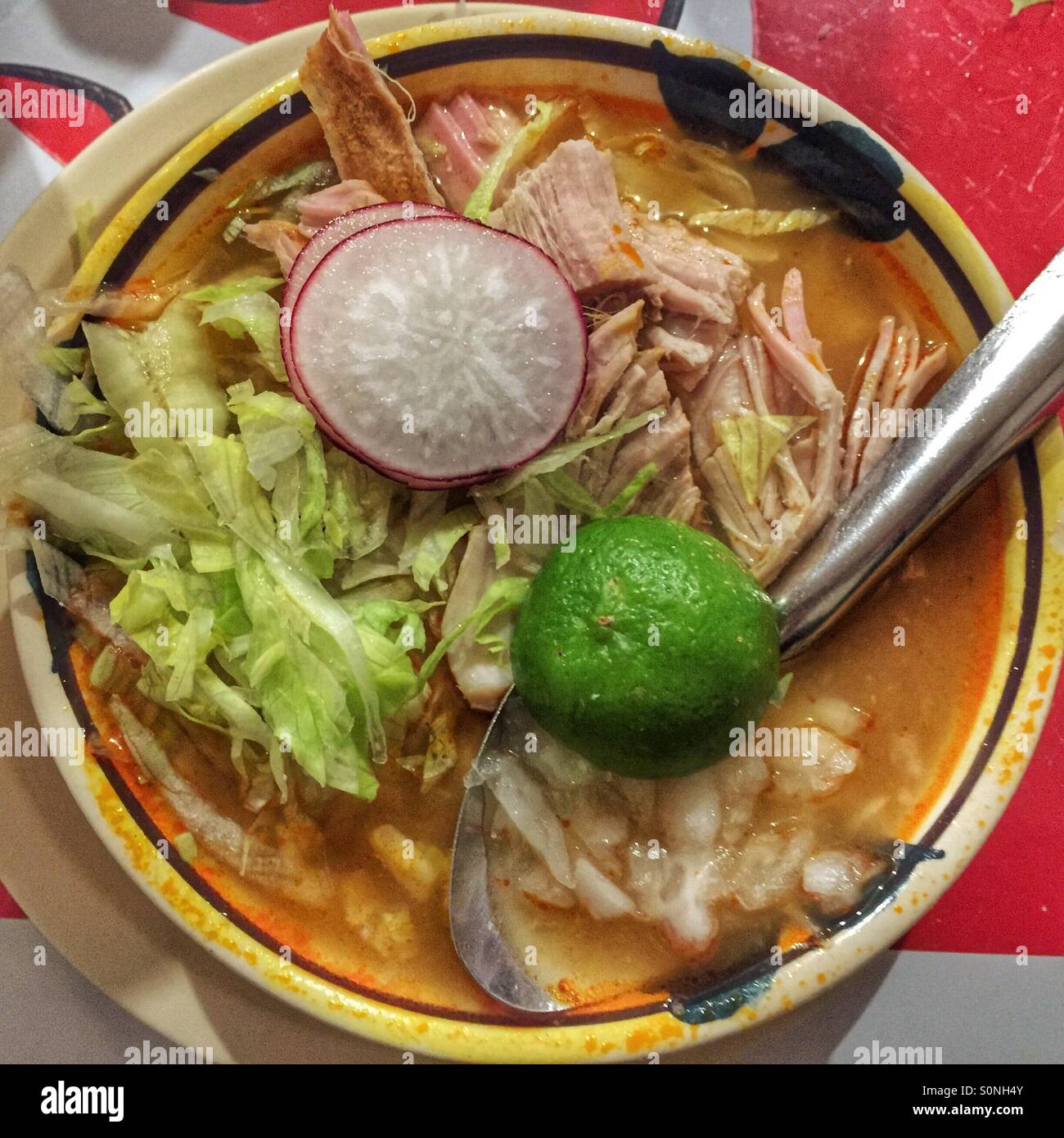 A delicious bowl of Pozole is topped with a lime and slices of radish. Stock Photo