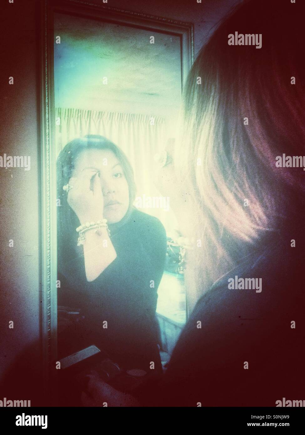 A lady uses a mirror to apply makeup. - Smartphone Captured Stock Image