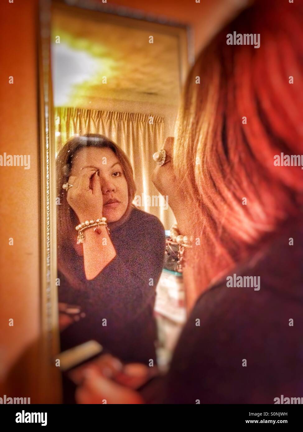 A lady uses a mirror to apply makeup. - Smartphone Captured Stock Image