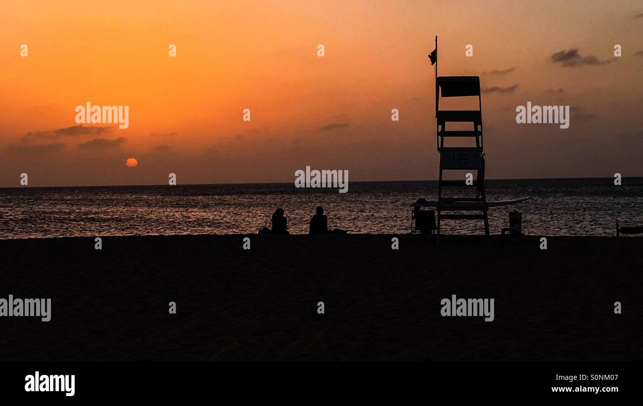 Sunset on the beach of Sal Cape Verde with lifeguard station and people sitting in the sand watching the sunset - Smartphone Captured Stock Image