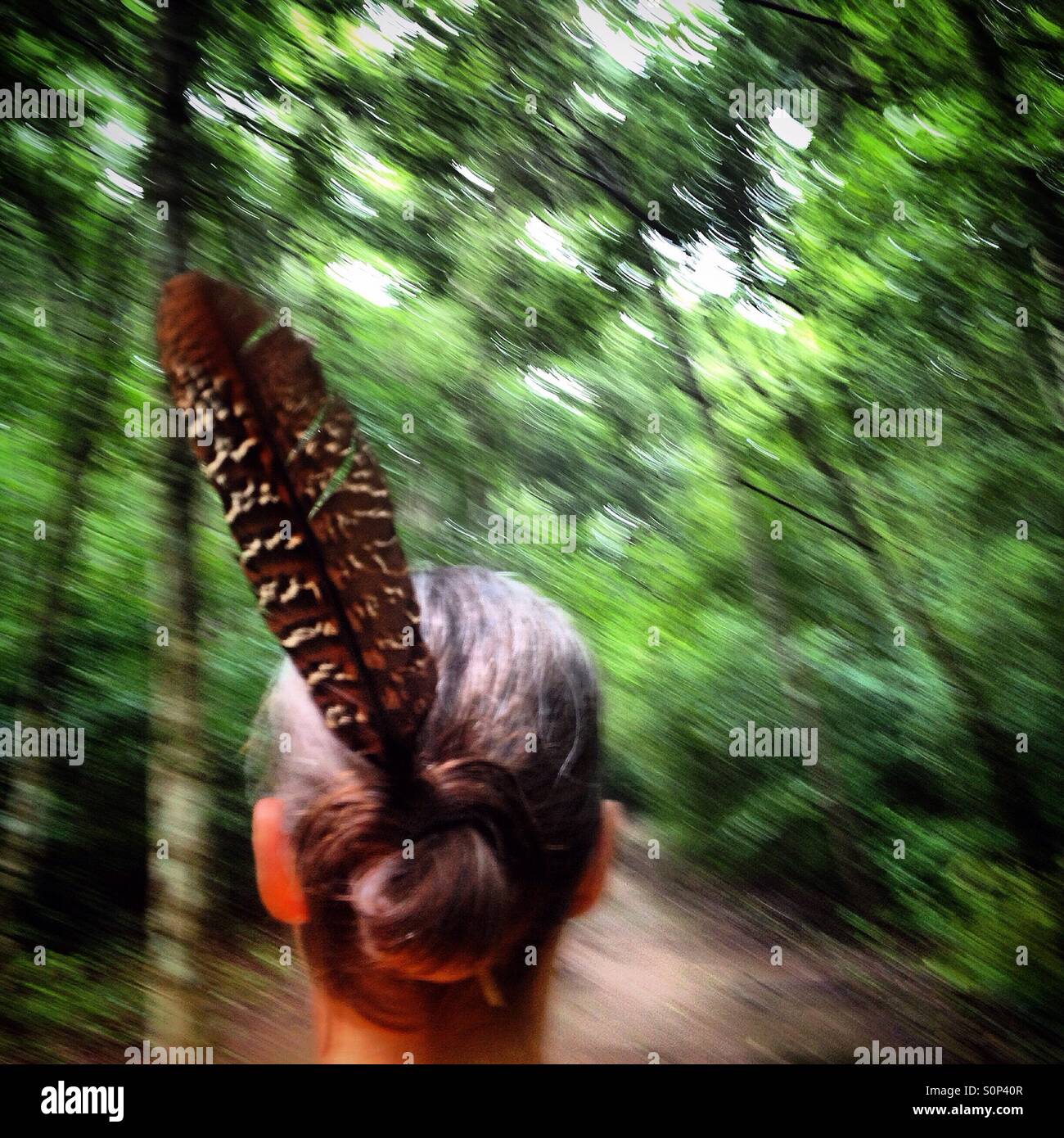 A woman wearing a bird feather walks in the jungle in the Mayan city of Mirador, Peten, Guatemala - Smartphone Captured Stock Image