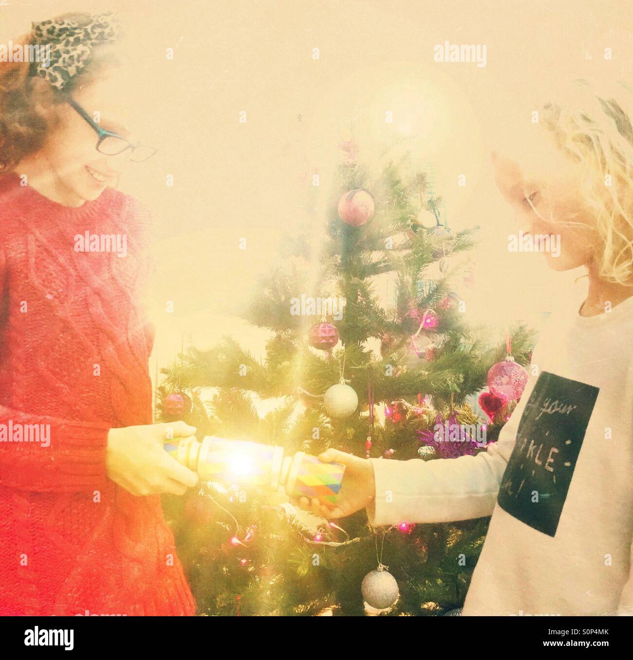 Two young children pulling a Christmas cracker in front of the Christmas tree Stock Photo