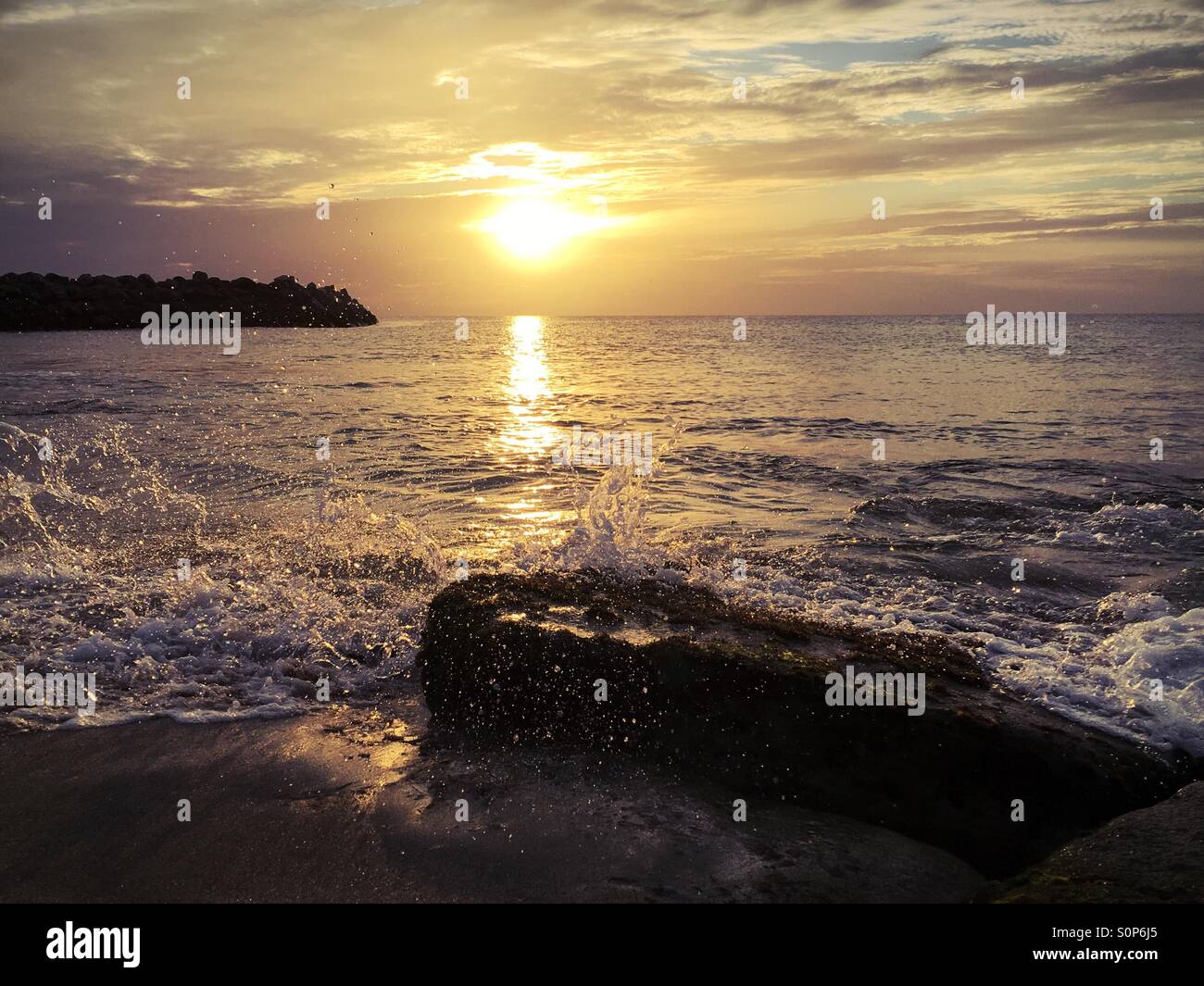 Golden hour sunset with waves crashing into a rock in the foreground - Smartphone Captured Stock Image