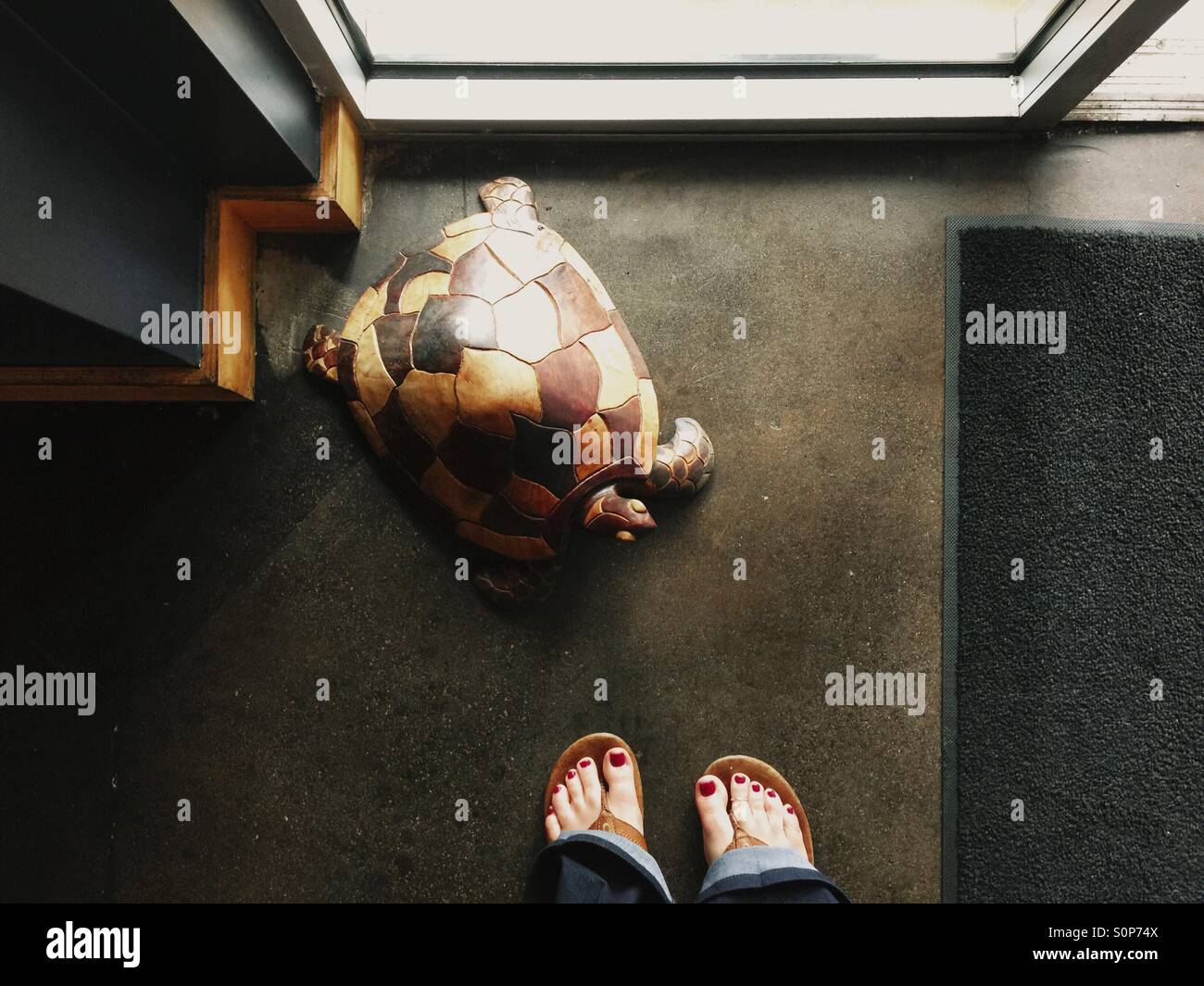 Feet in flip flop by wooden turtle. Stock Photo