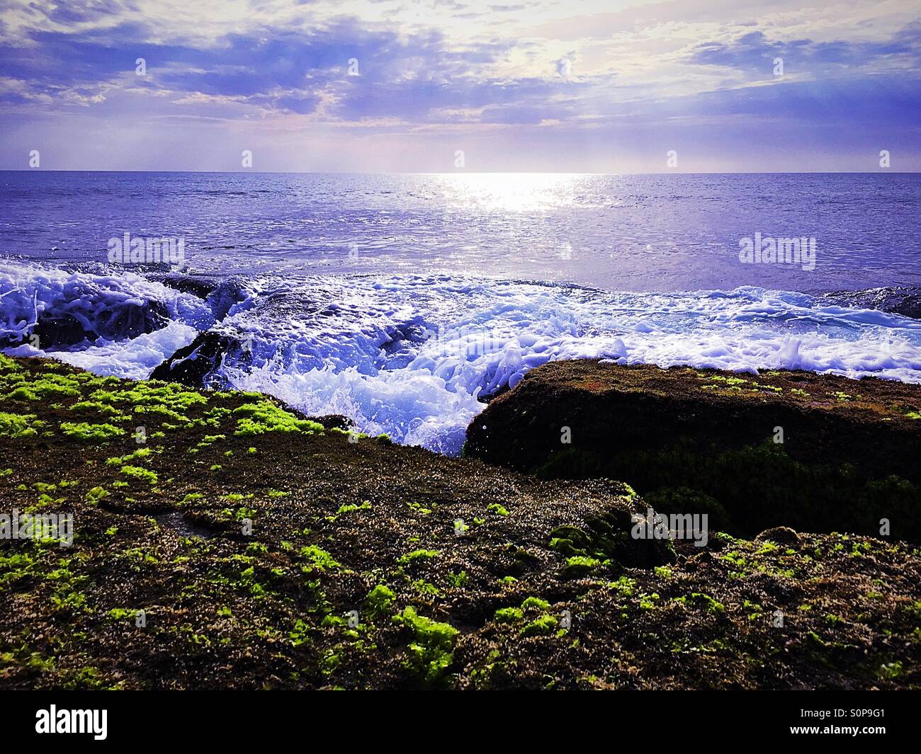 Foaming spray from waves of incoming tide towards rocks with sea weed - Smartphone Captured Stock Image