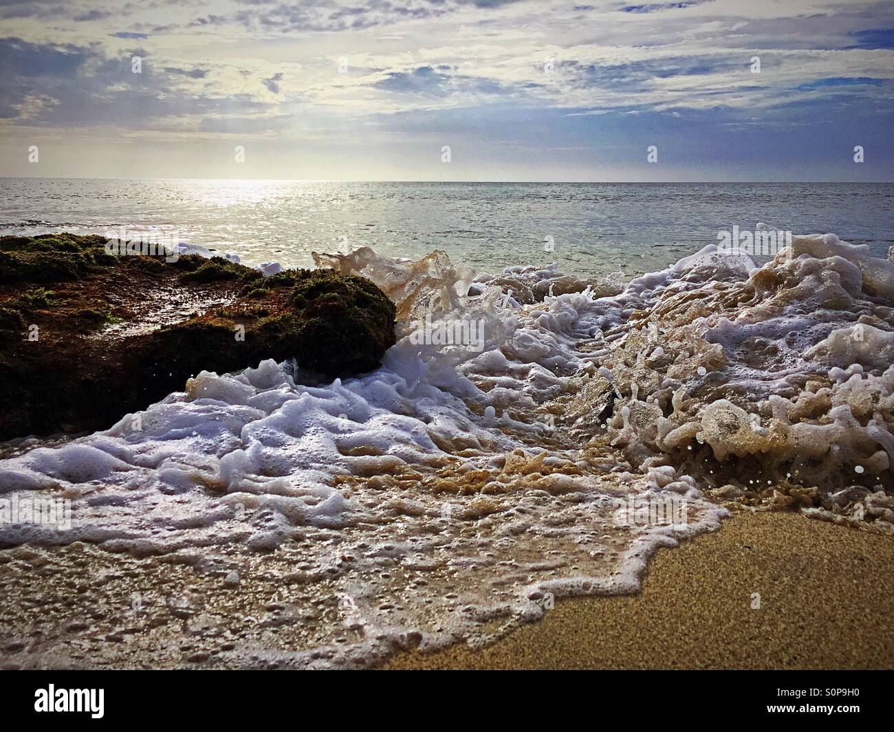 Sun reflecting on the ocean with tide coming in and sea swirling round rocks - Smartphone Captured Stock Image