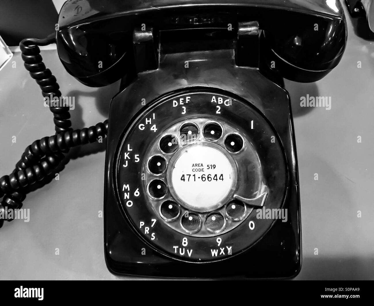 Rotary phone, black, with phone number, still usable, sitting on a table. Receiver on the cradle. - Smartphone Captured Stock Image